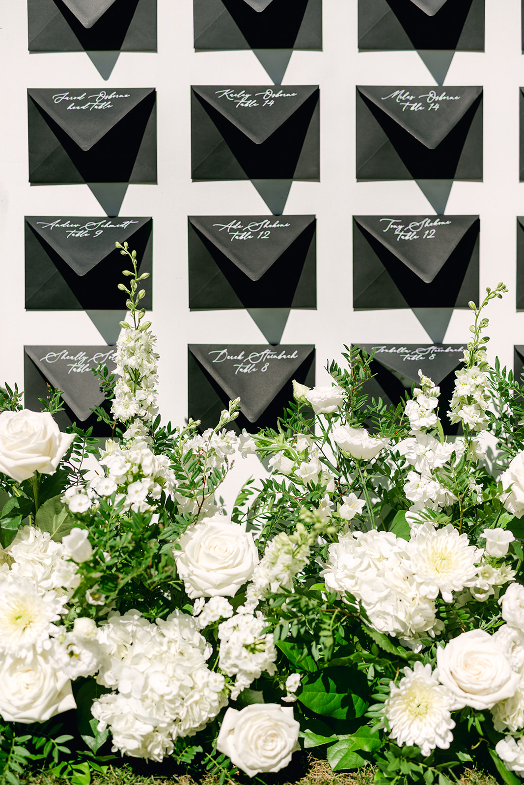 Unique wedding seating chart with handwritten notes to each guest in black envelopes surrounded by all white flowers