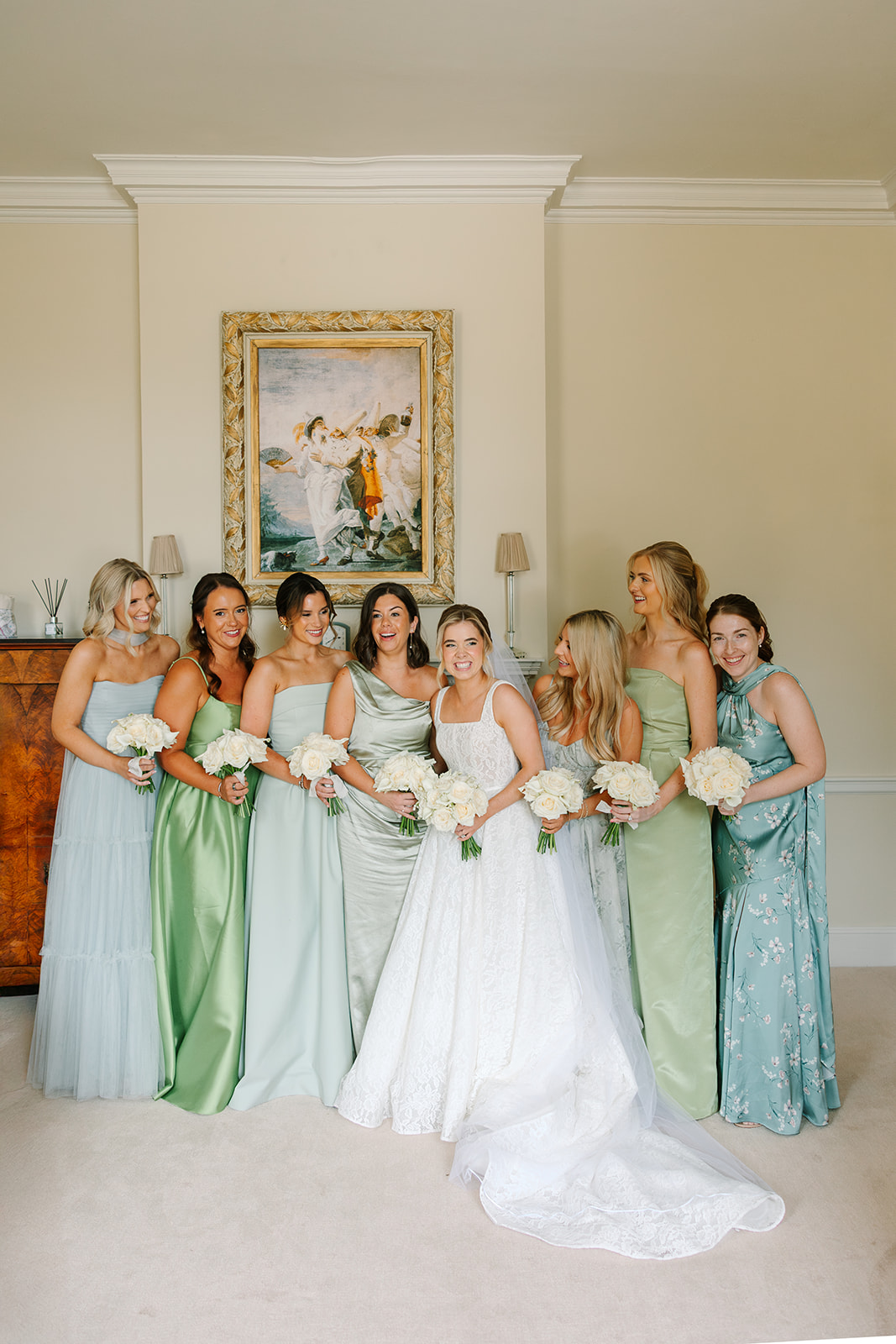 Bridesmaids wearing mismatched green and blue dresses and bride wearing a lace gown with square neckline