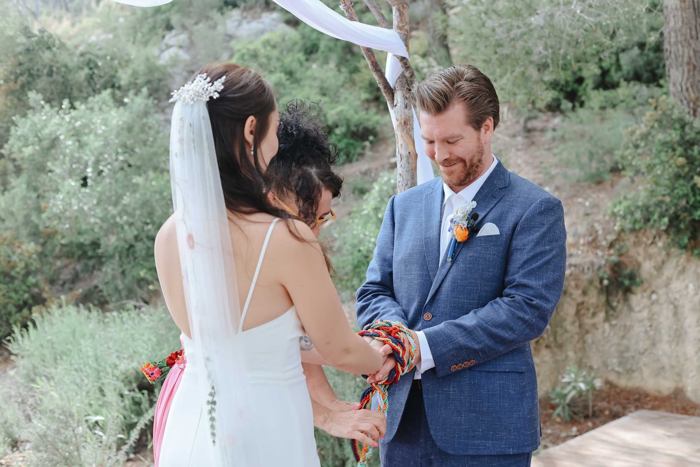Bride and groom doing a handfasting ritual as part of their outdoor wedding ceremony