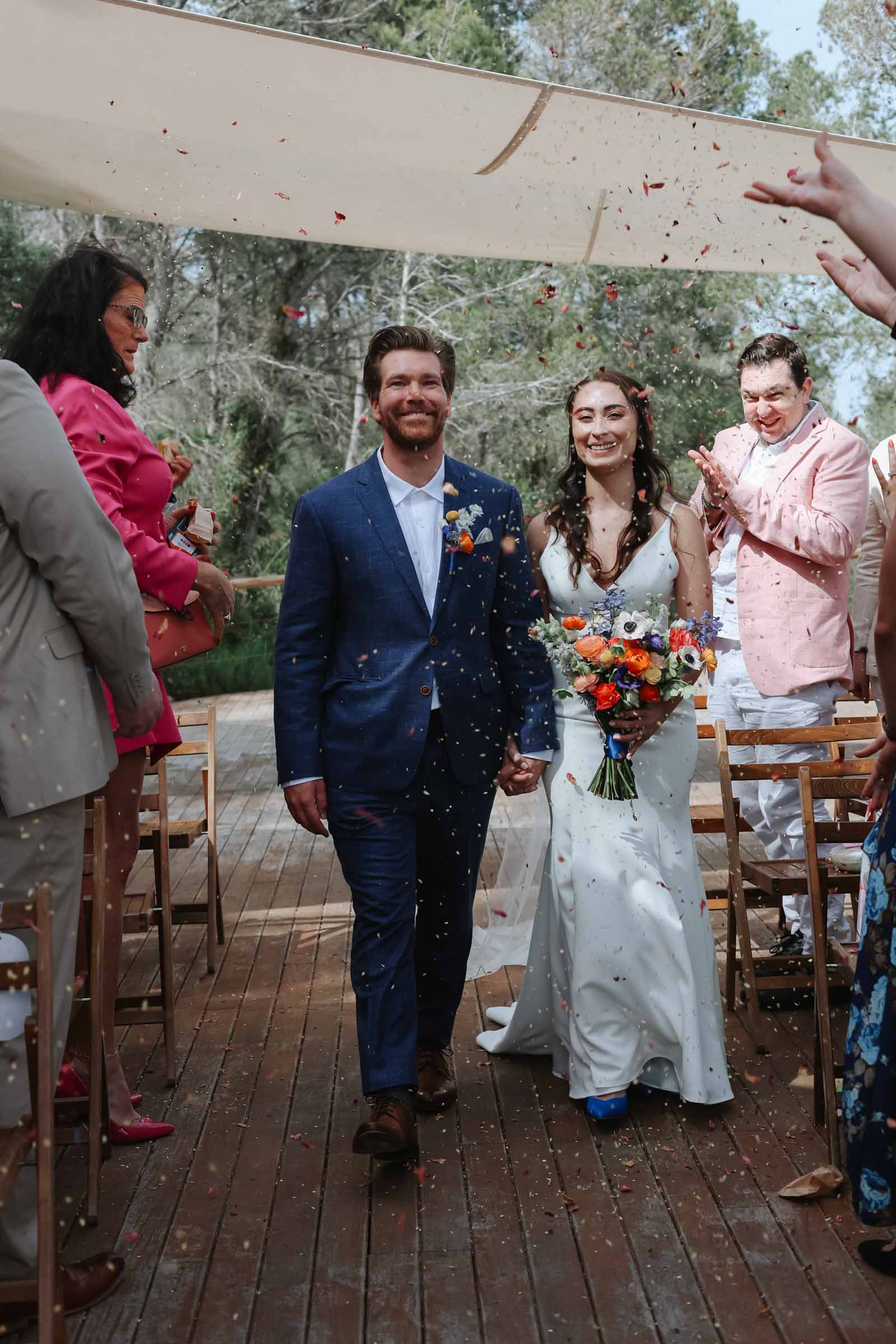 Bride and groom walking down the aisle with guests tossing flower petal confetti to celebrate