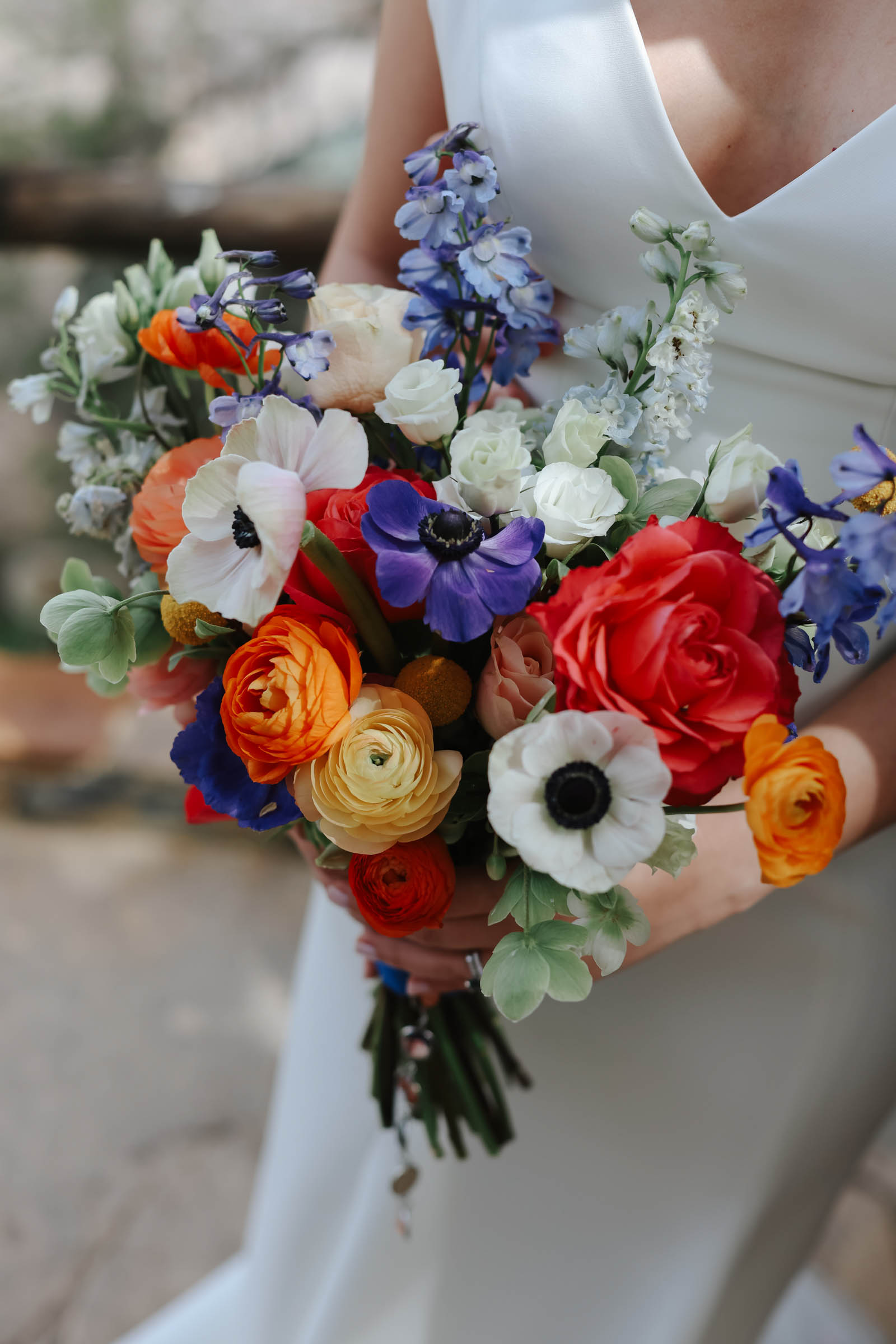 A colorful wedding bouquet with purple and white anemones and orange, red, and yellow ranunculus.