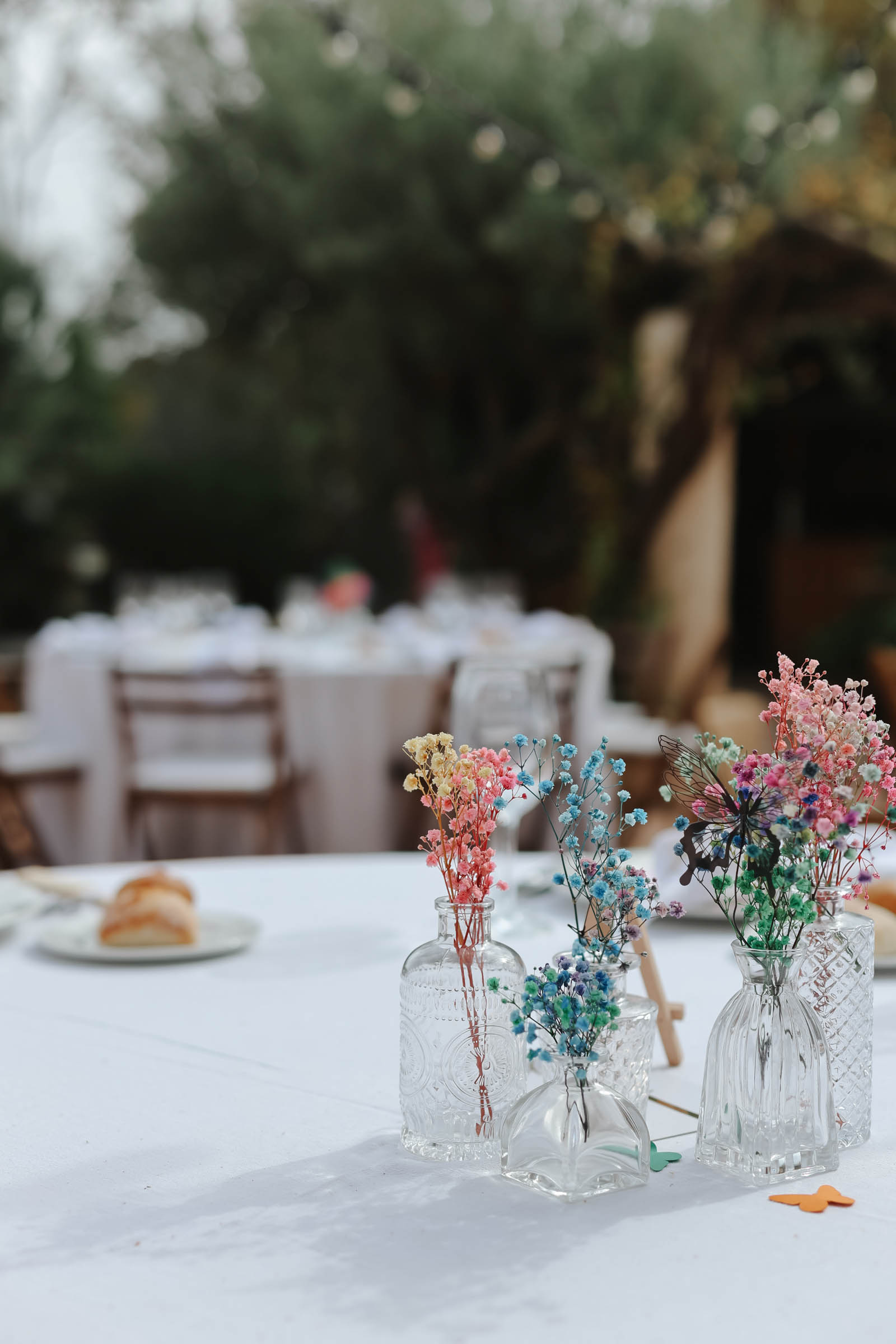 Colorful rainbow dyed Gypsophila or babys breath in mismatched vintage bud vases with butterly cutouts for simple wedding centerpiece