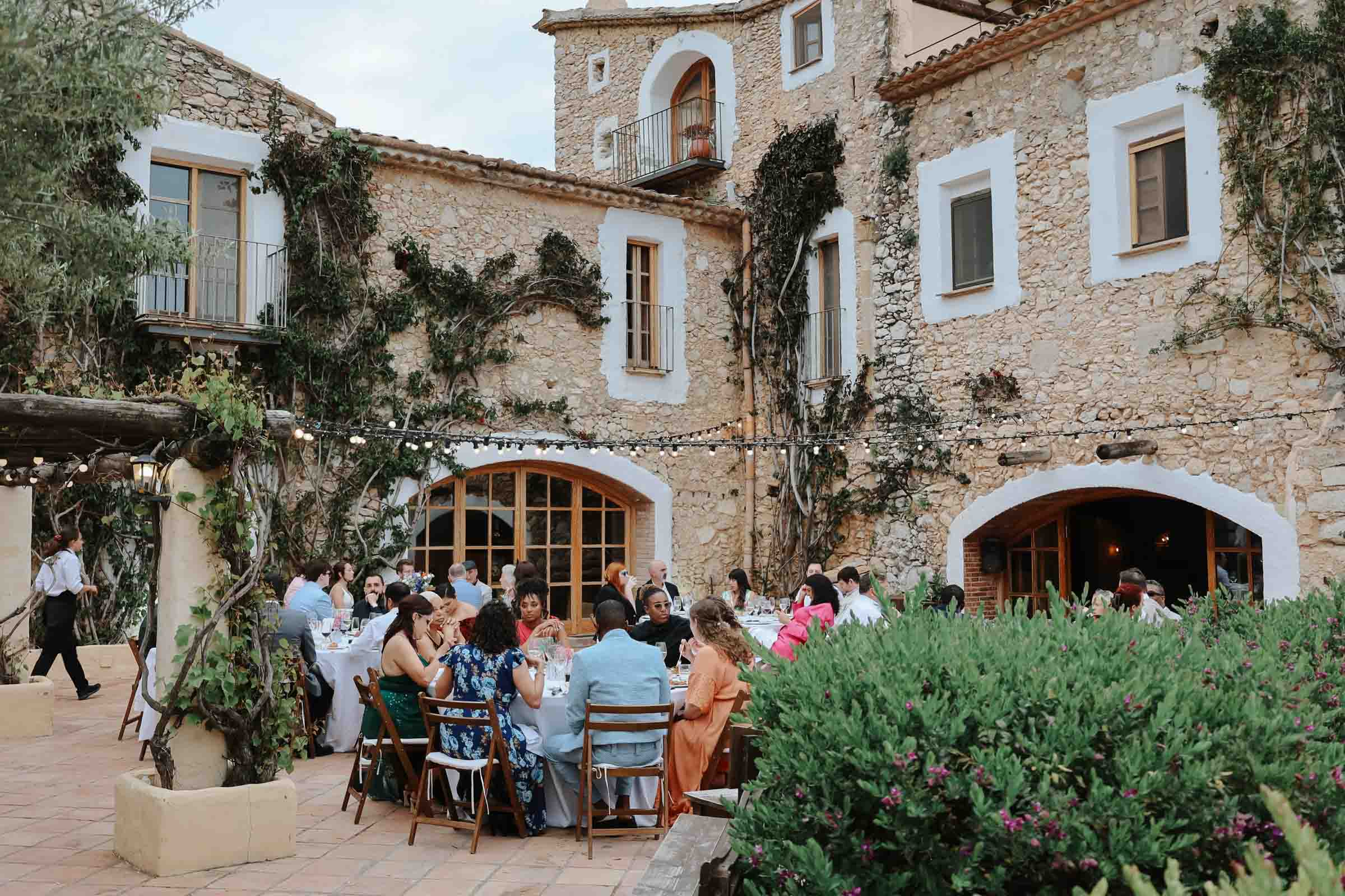 Outdoor patio wedding reception with hanging bistro lights against a stone building