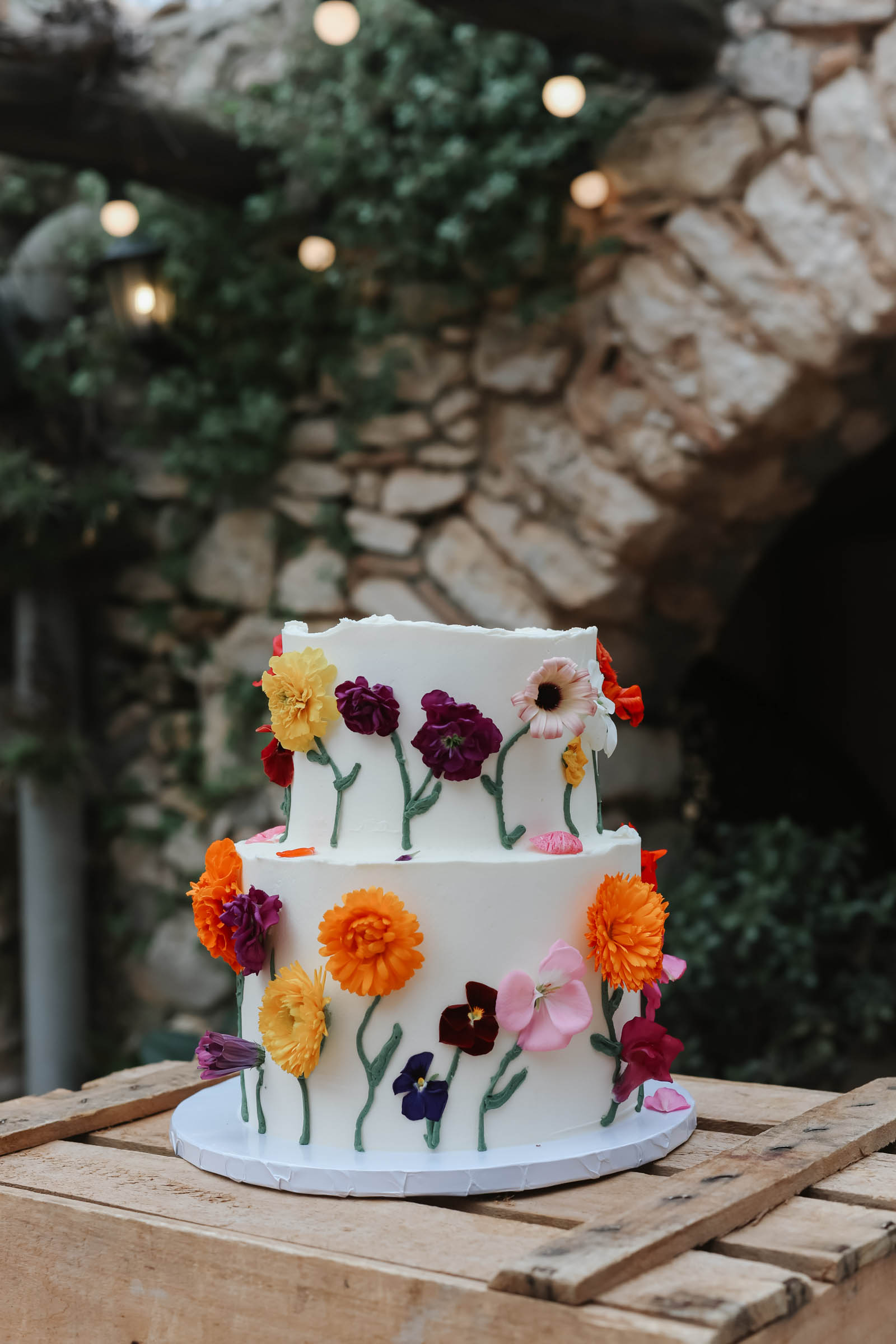 Two tiered white wedding cake decorated with real colorful pansy and daisy flowers