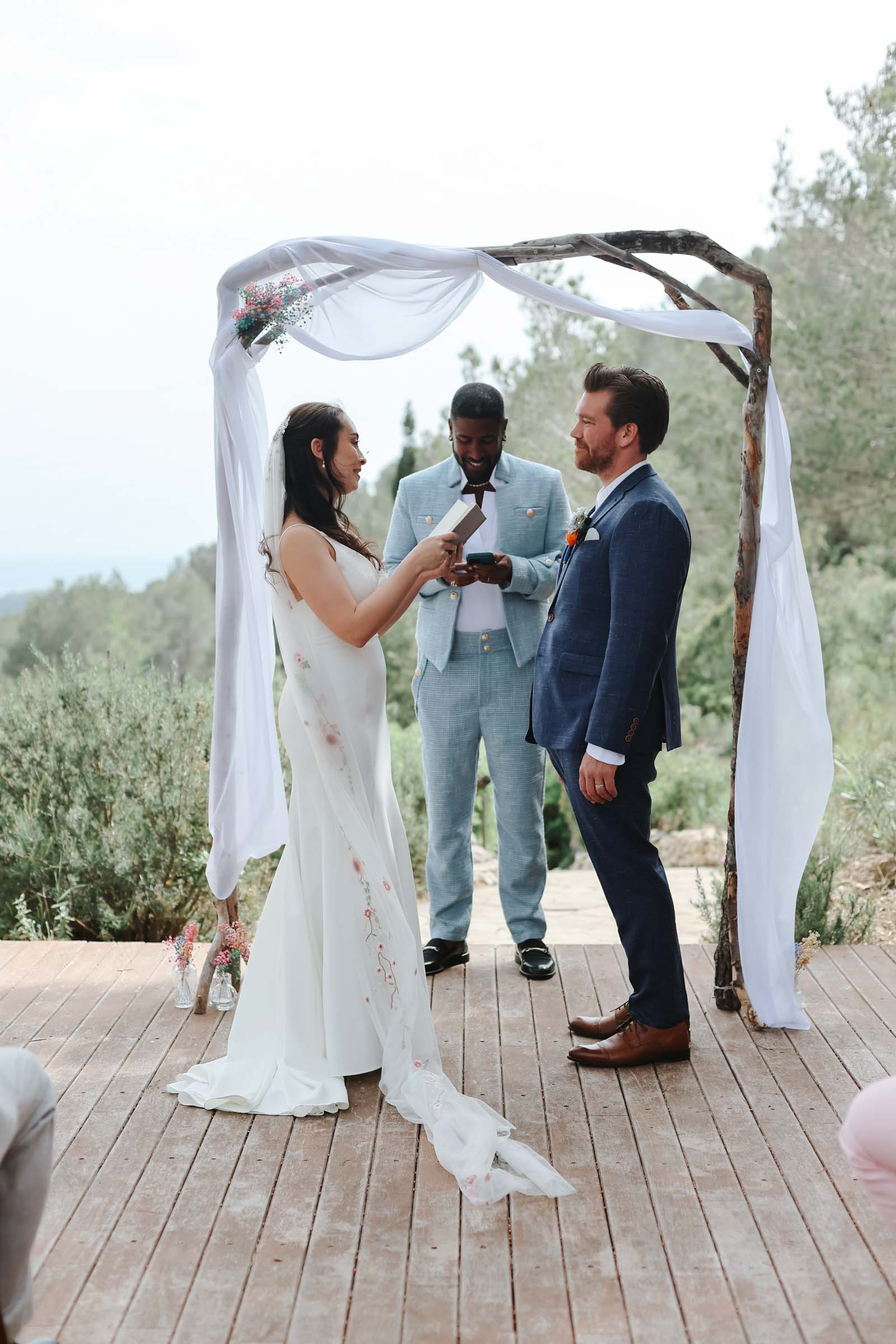 Bride and groom exchanging vows under a simple rustic wedding arch overlooking the Mediterranean at Almiral de la Font in Spain
