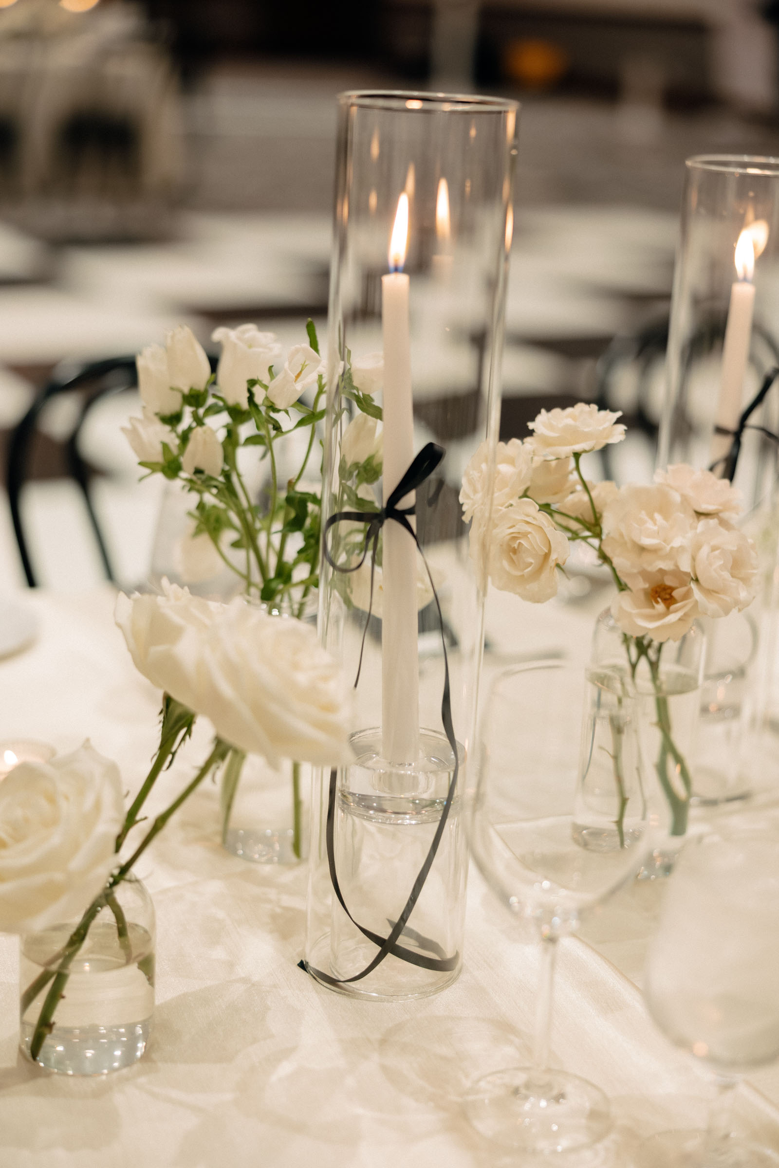 Long thin black ribbons tied around white candlesticks for wedding table decor
