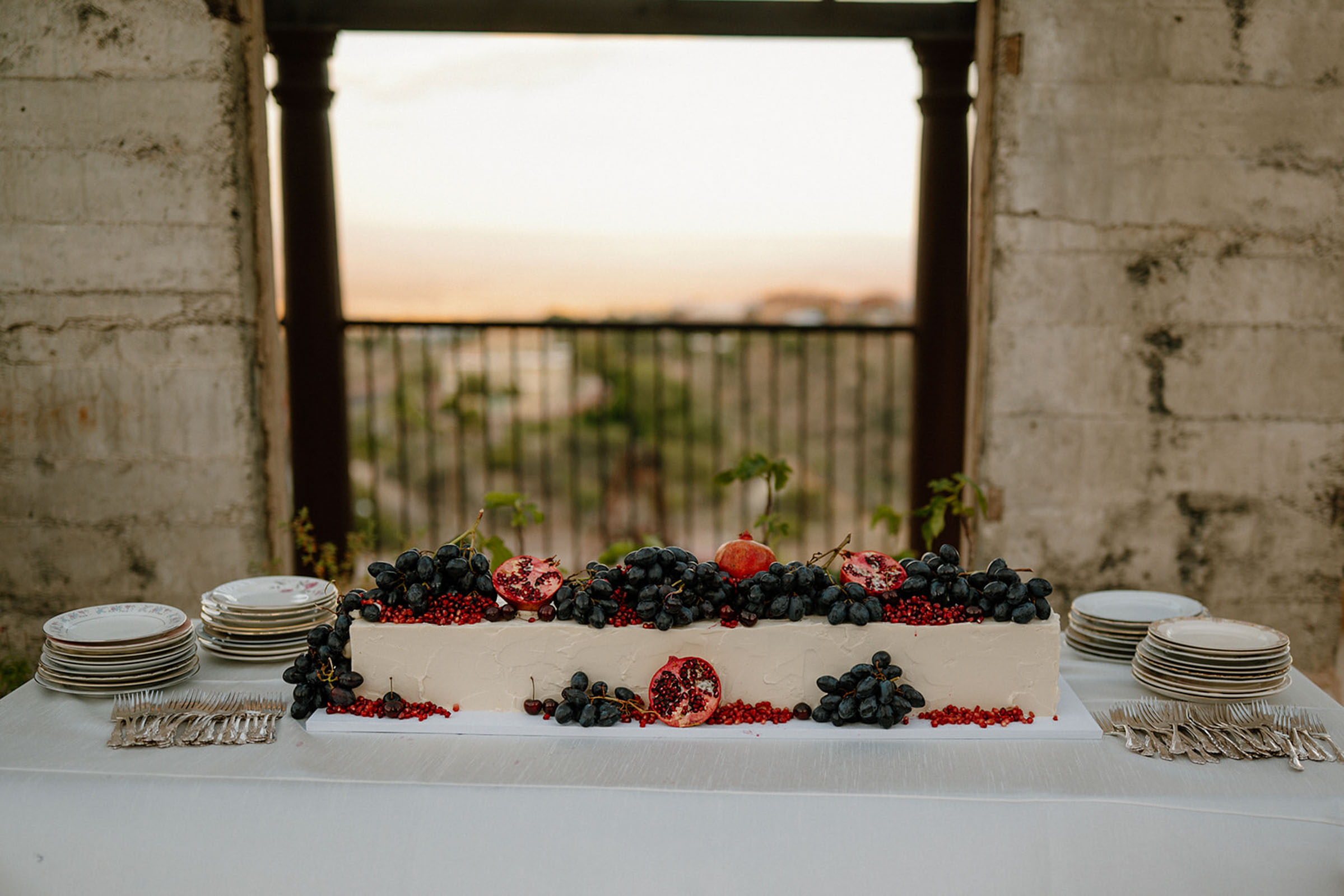 Long white wedding cake decorated with grapes and pomegranate fruits