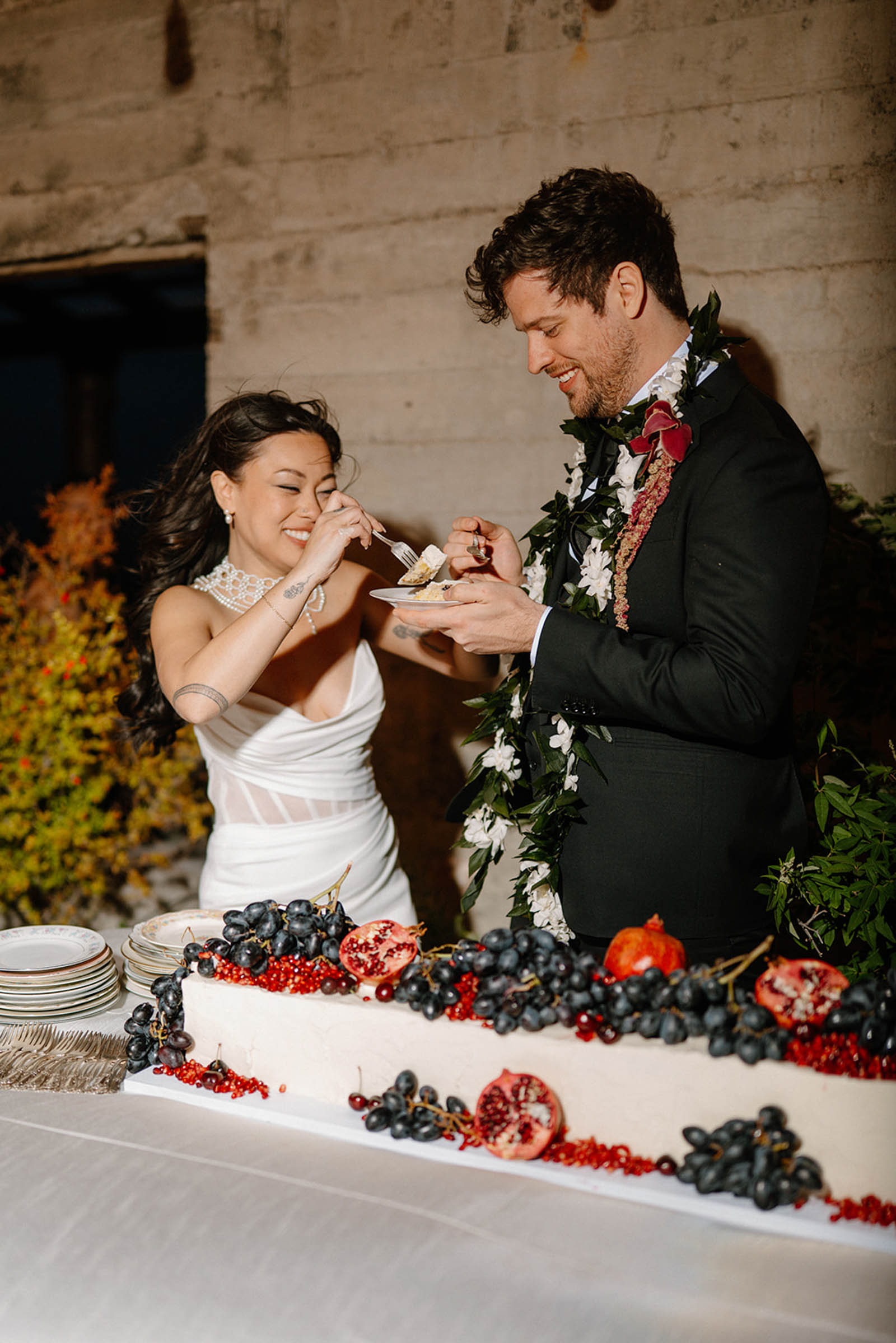 Long white wedding cake decorated with grapes and pomegranate fruits