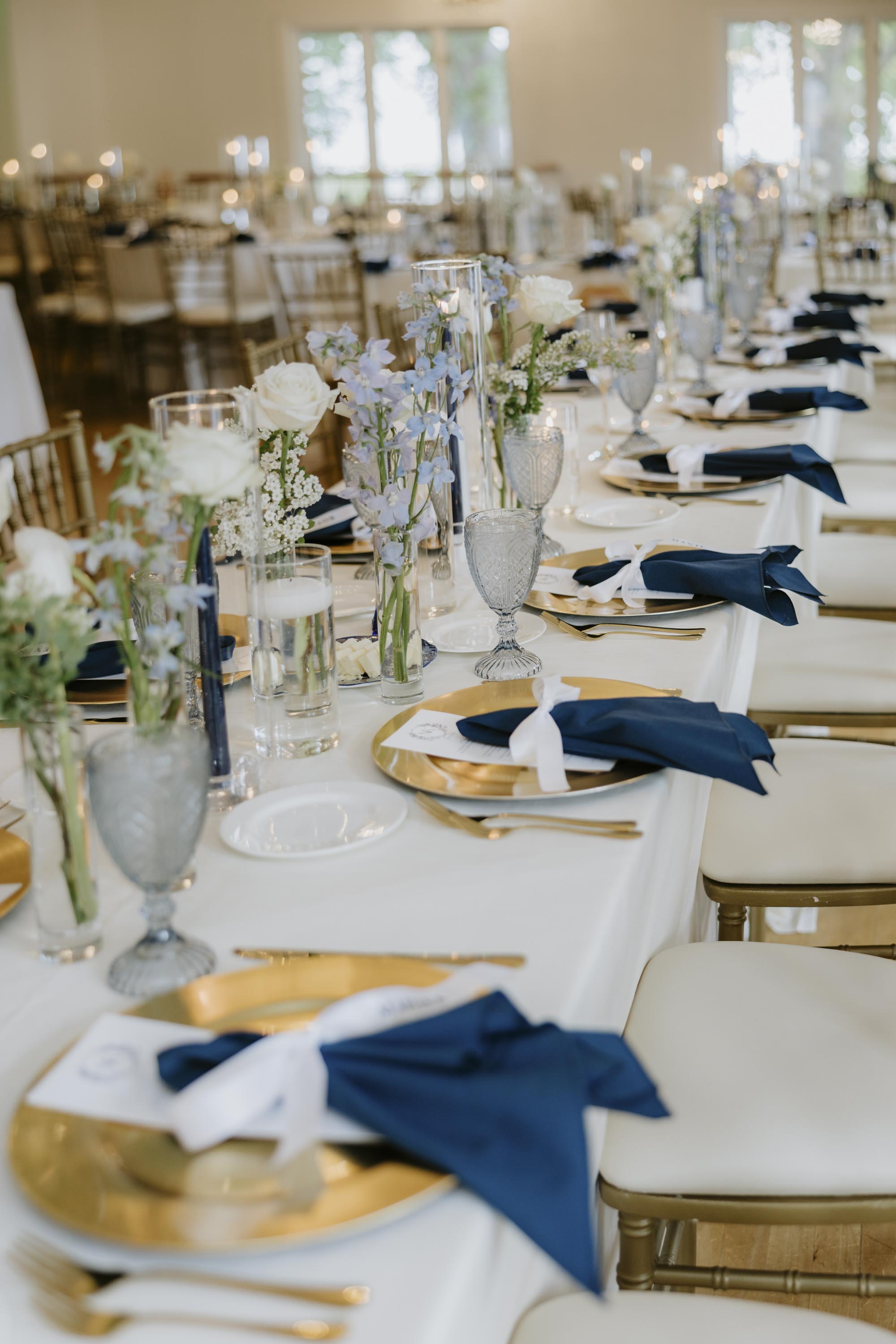 Long reception table with navy blue napkins and small floral and candle centerpieces
