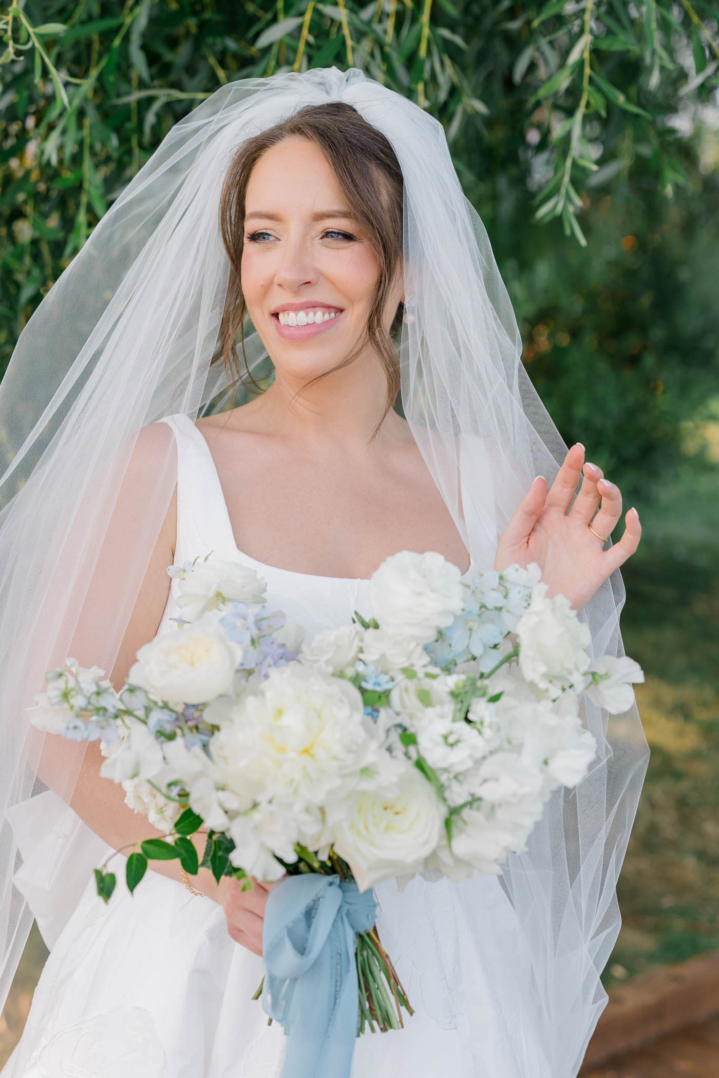 Bride wearing square neckline wedding dress and a long cathedral wedding veil holding blue and white flowers