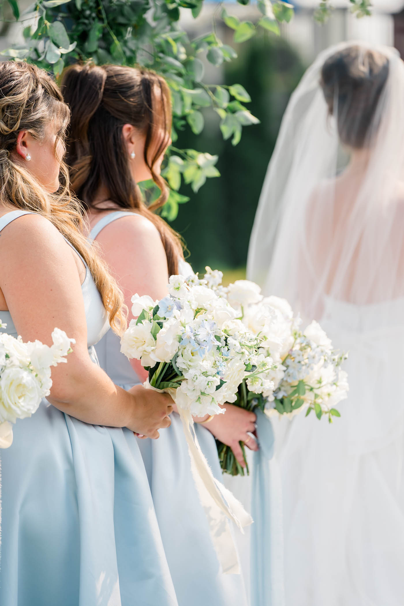 Bridesmaids in baby blue Dessy dresses holding white bouquets during wedding ceremony