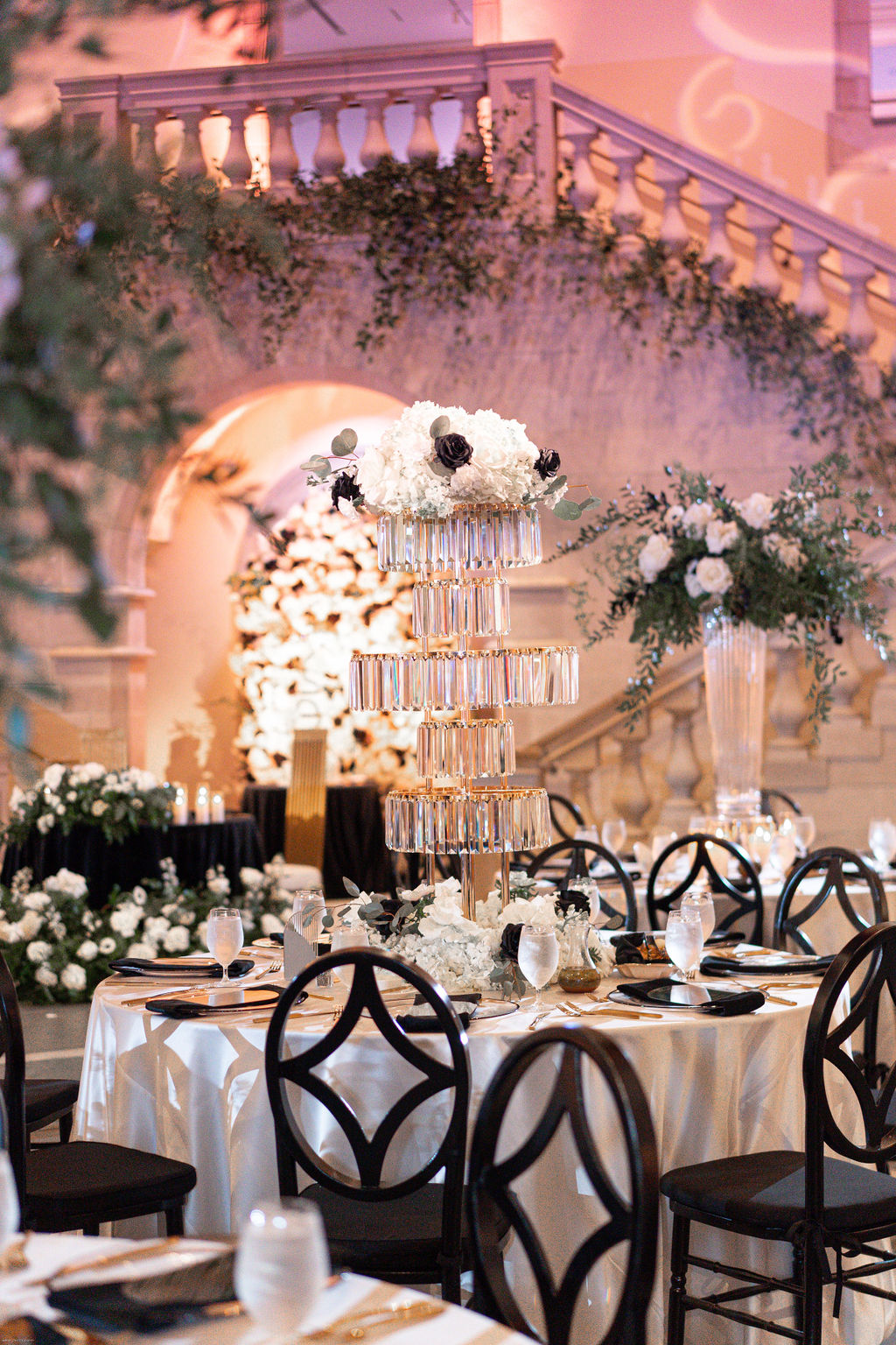 Tall acrylic and gold chandelier centerpiece with white and black flowers on a table with white velvet linens