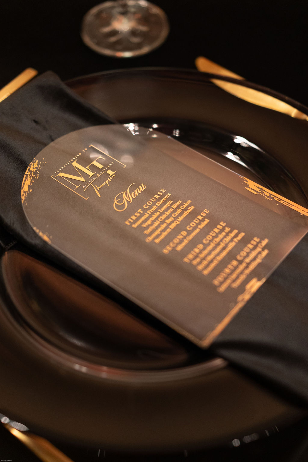 Arch shaped acrylic wedding menus with gold lettering on top of black velvet napkin