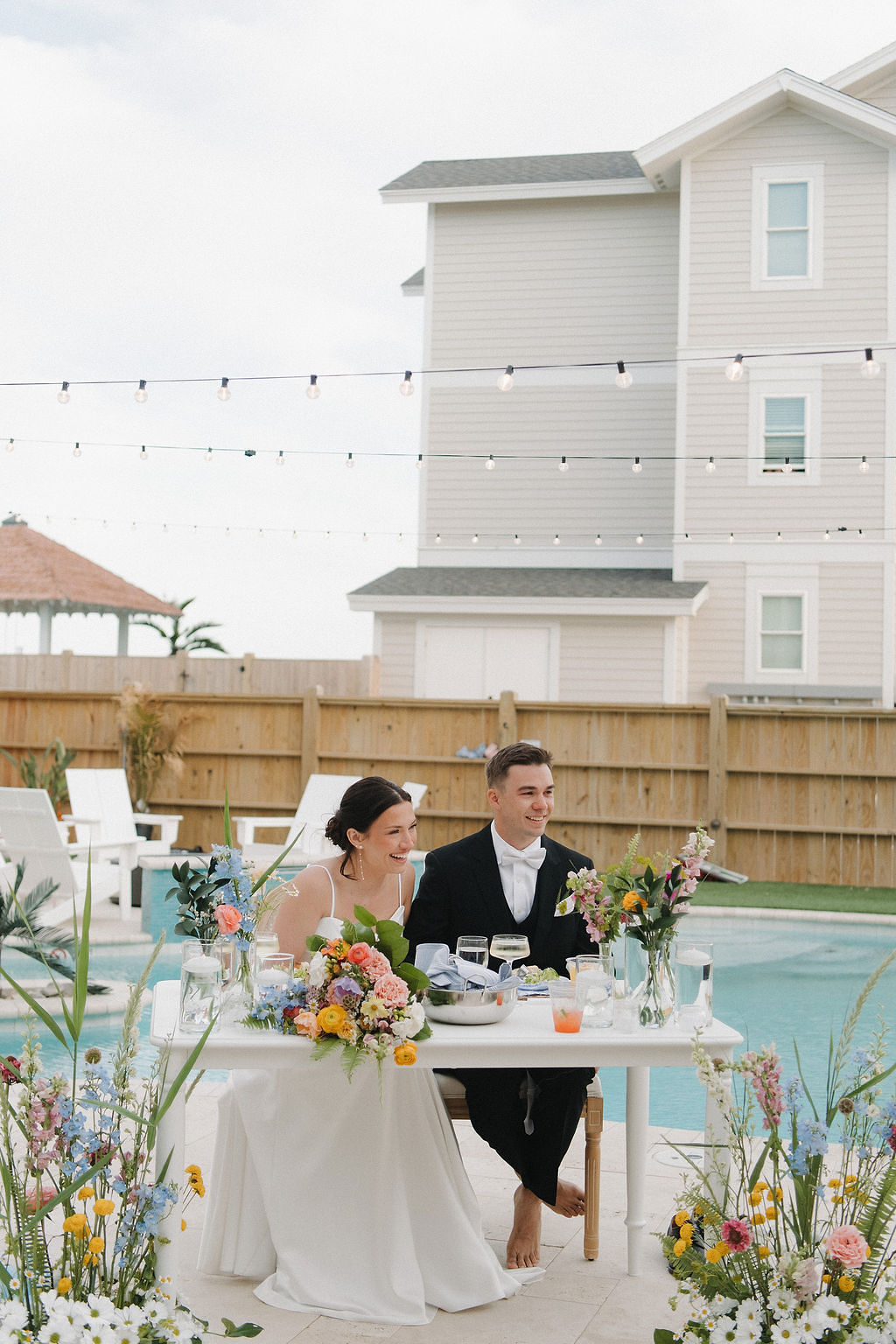 Barefoot bride and groom at their sweetheart table near the pool at a beach house wedding venue