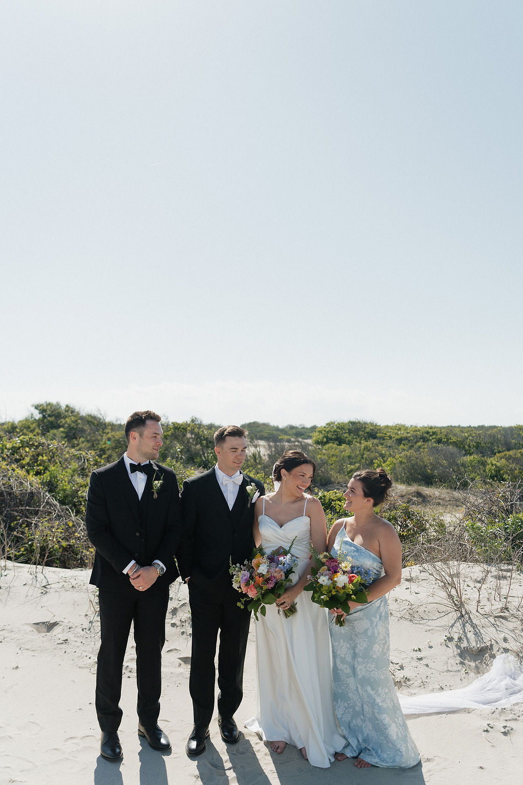 Beach bride and groom with their groomsman and bridesmaid wearing a blue and white floral dress
