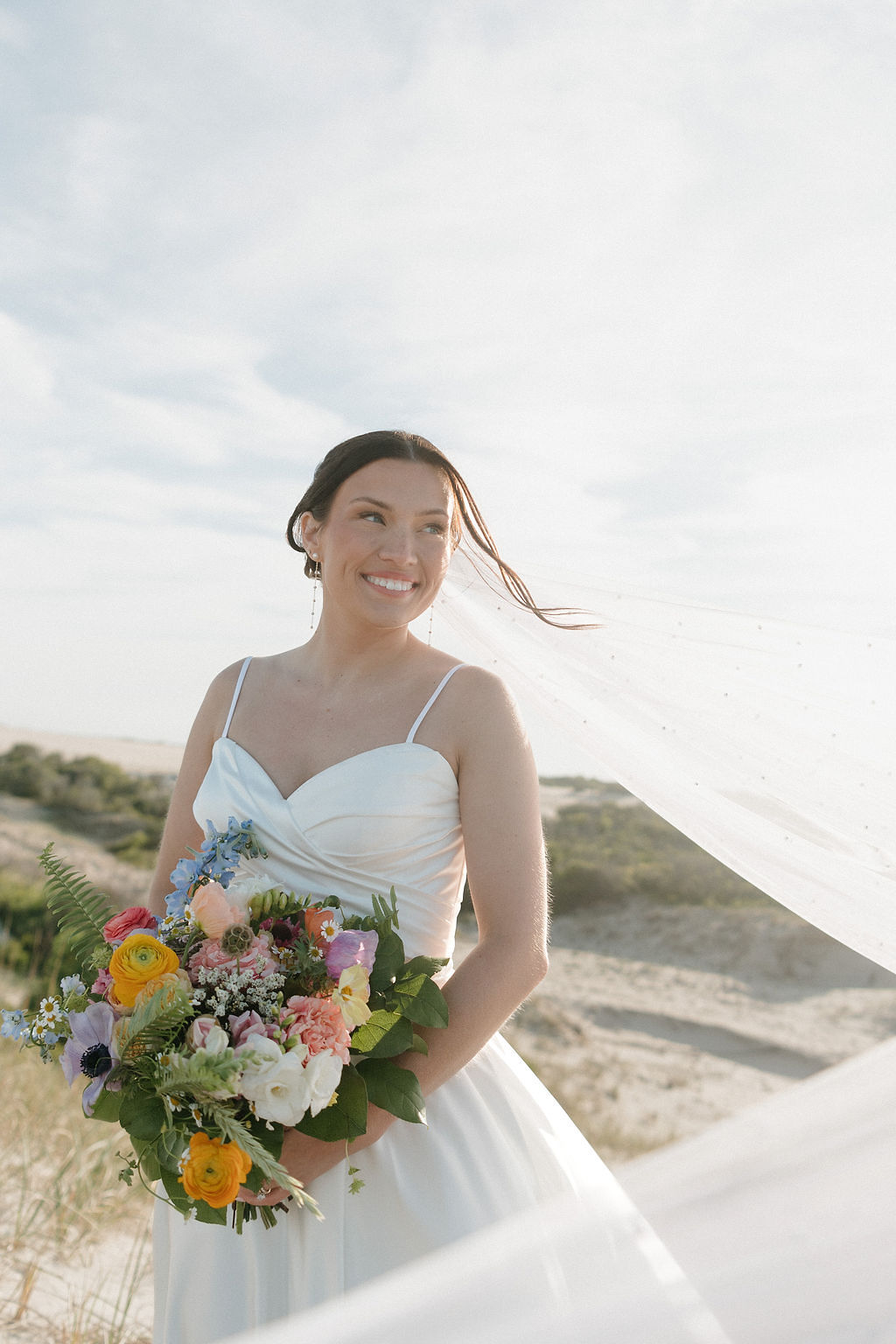 Beach bride with beaded pearl veil holding a pastel colorful bouquet