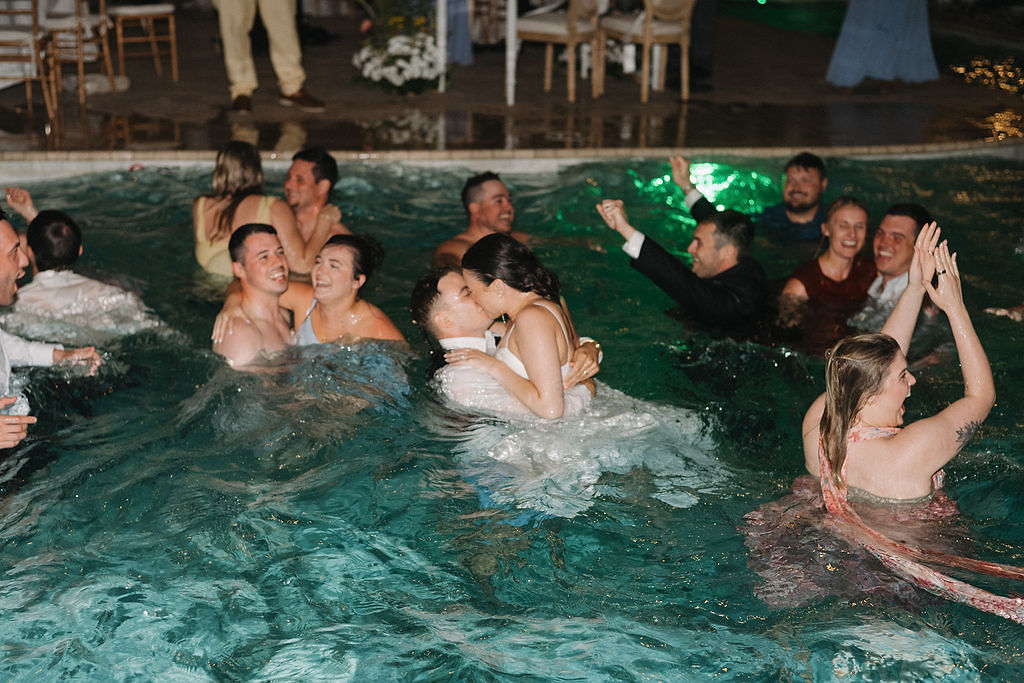 Bride and groom swimming in the beach house pool with their wedding guests at Hill Runner in Corolla