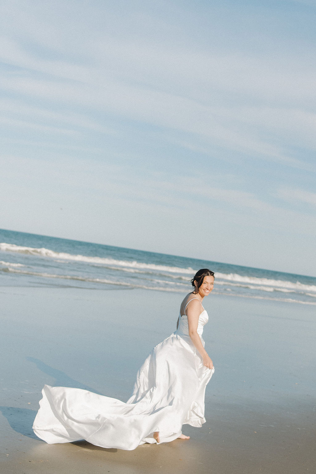 Carefree bride running on the Corolla beach in her wedding dress