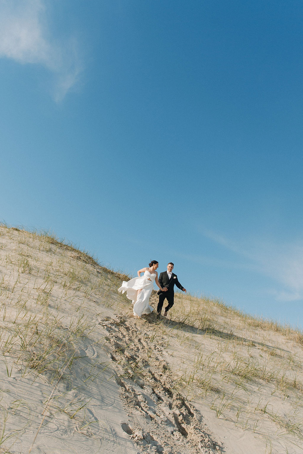 Bride and groom running down sand dunes in Corolla