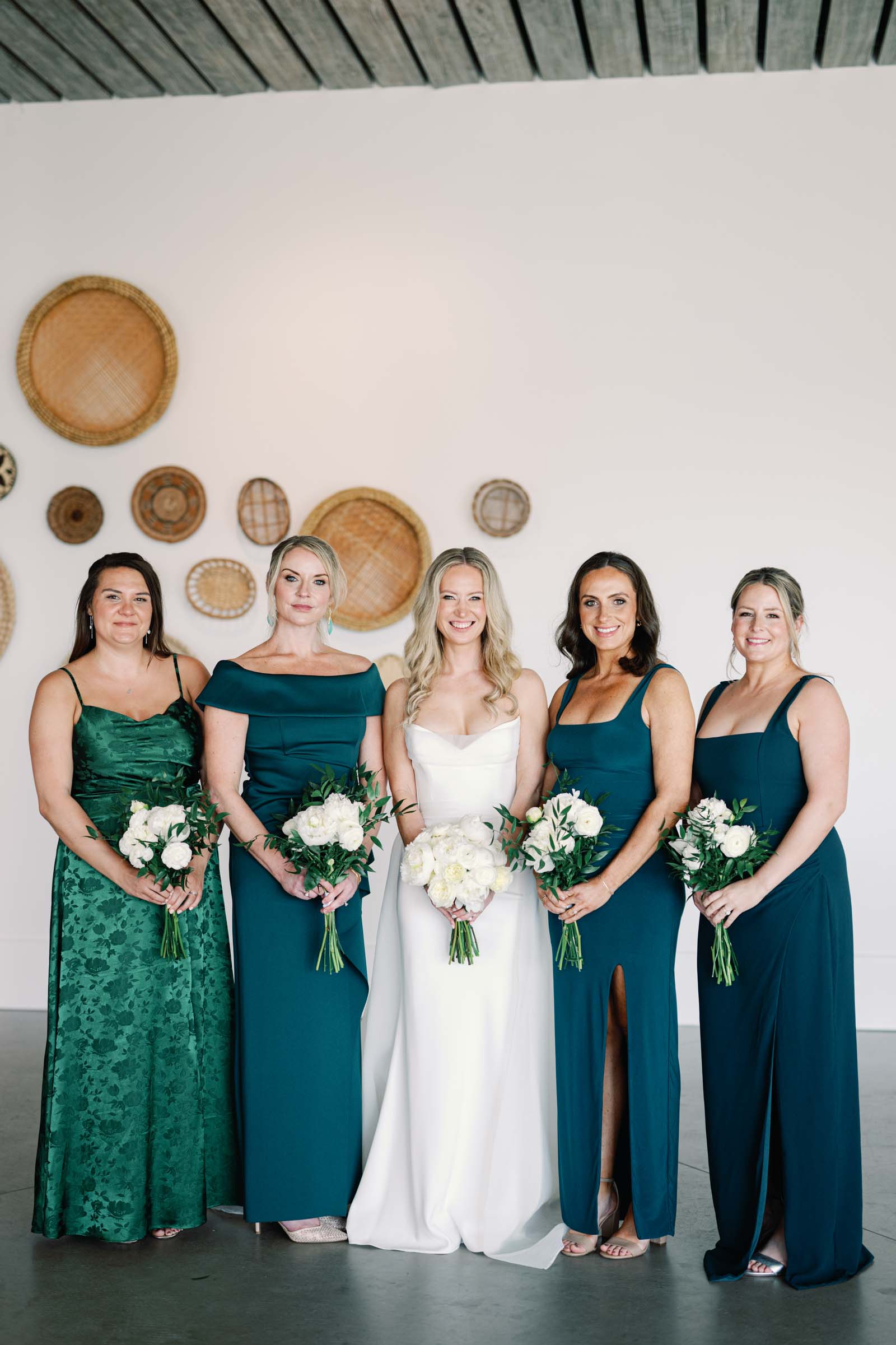 Bride and her bridesmaids wearing shades of green dresses while holding all white wedding bouquets