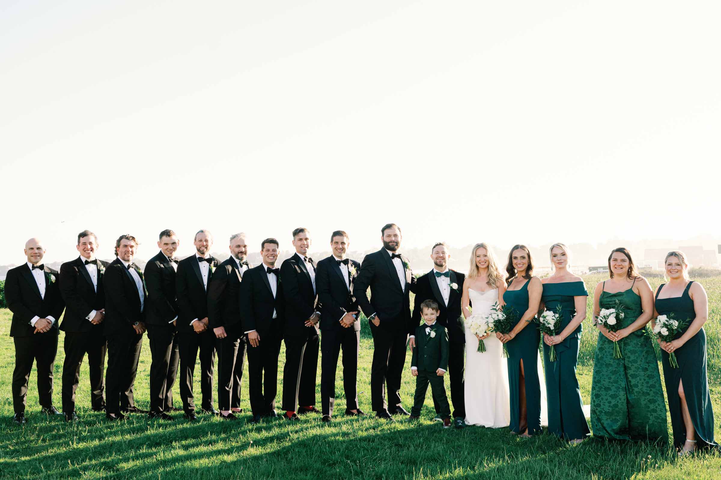 Large wedding party with groomsmen in tuxedos and bridesmaids in green dresses