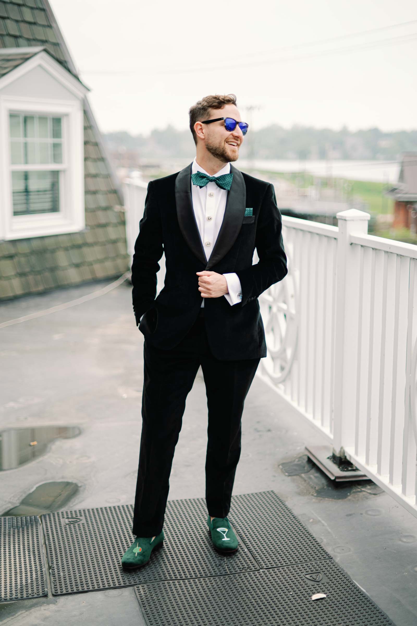 Groom wearing black velvet tuxedo with green bow tie and martini themed loafer shoes