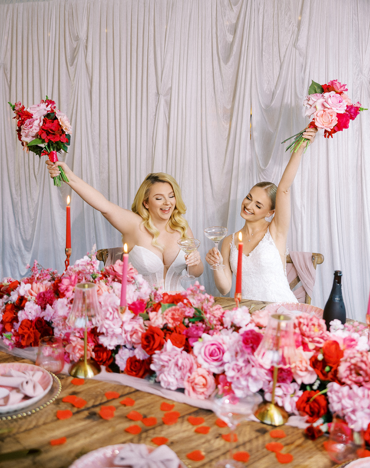 Two brides cheering with their pink and red wedding bouquets held up