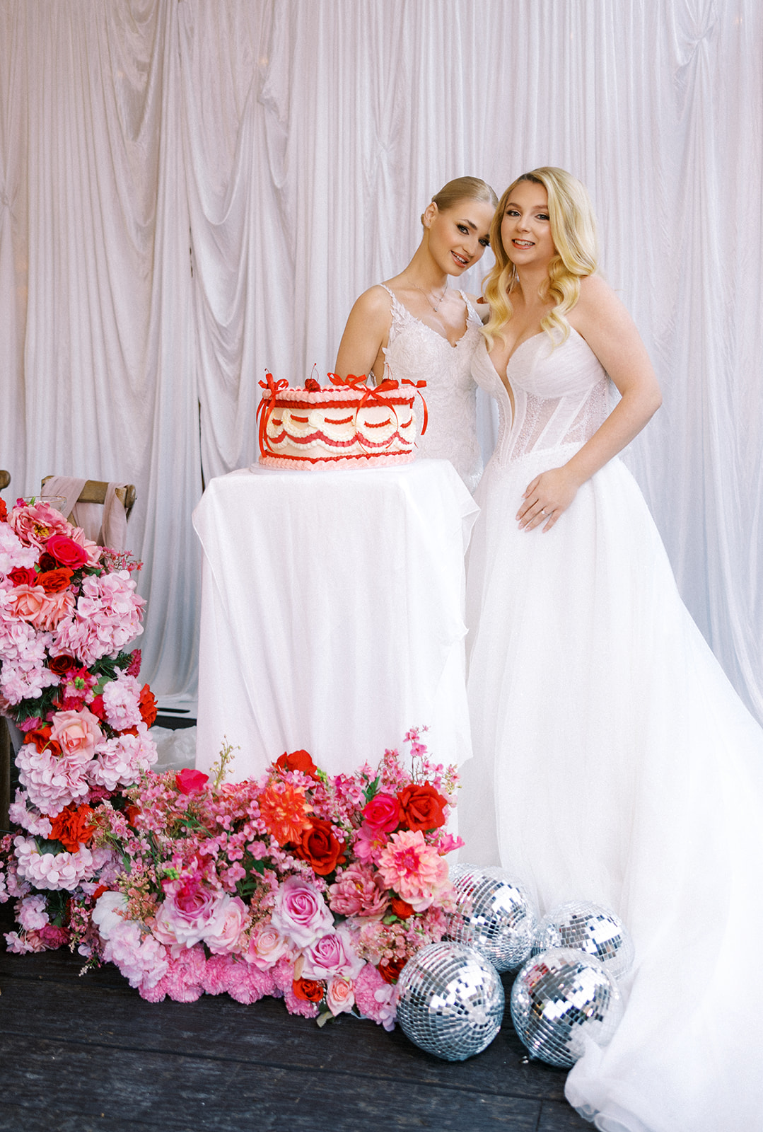 Two brides having a sweet moment during the pink and red wedding reception at The Glasshouse in Kent England