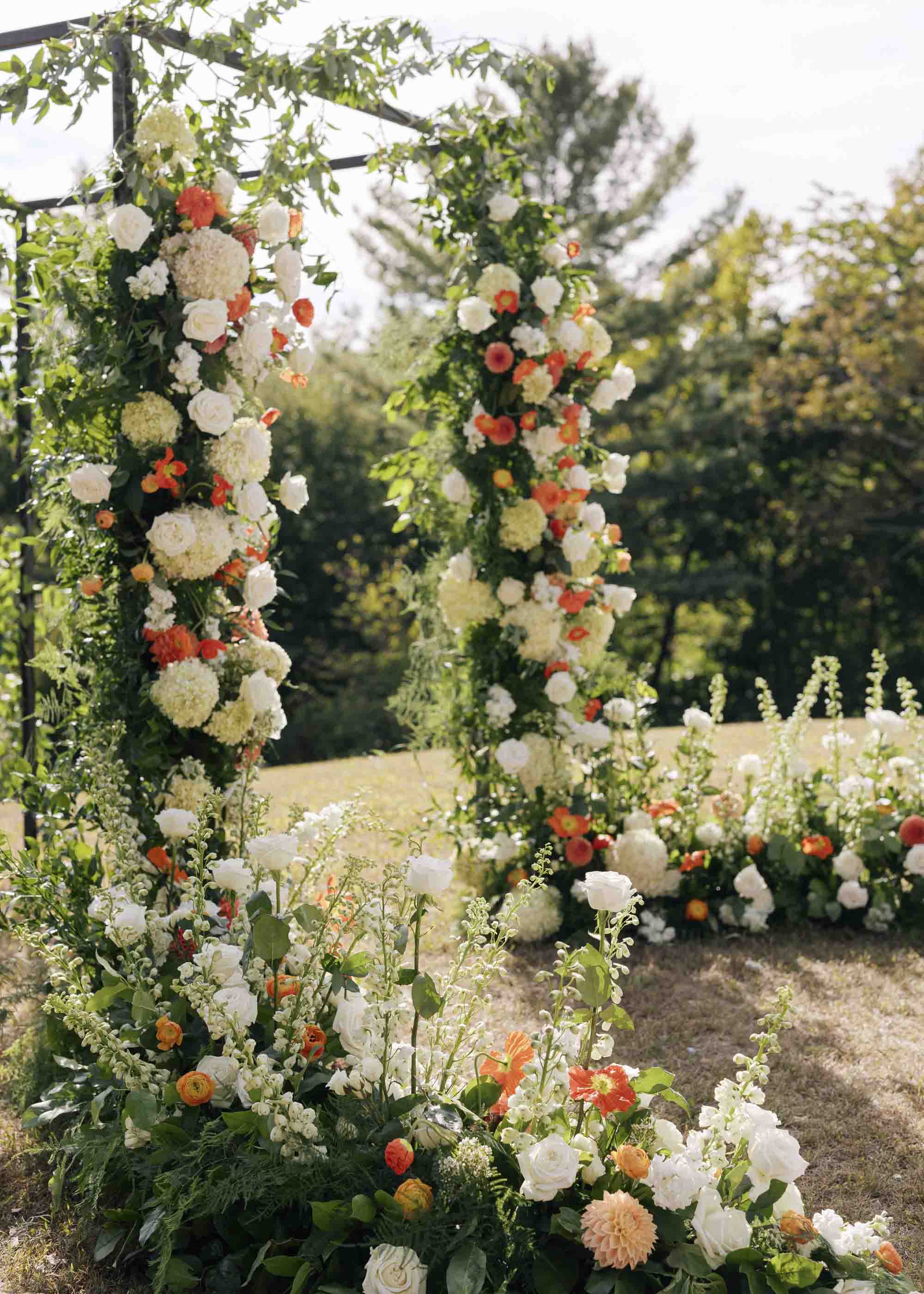 Lush orange and white flowers with poppies decorating outdoor wedding ceremony arch