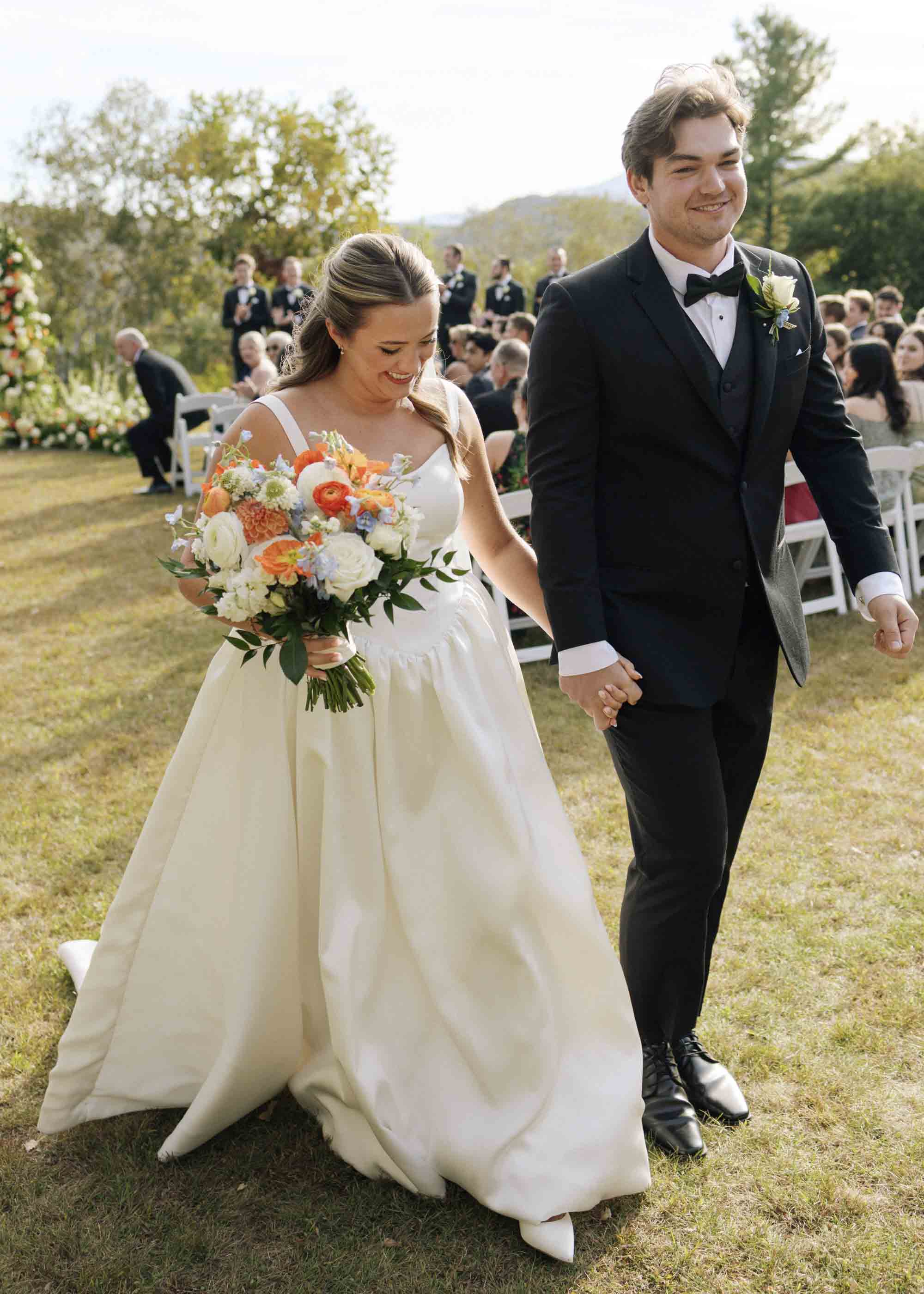 Bride carrying an orange white and blue wedding bouquet down the aisle in Vermont
