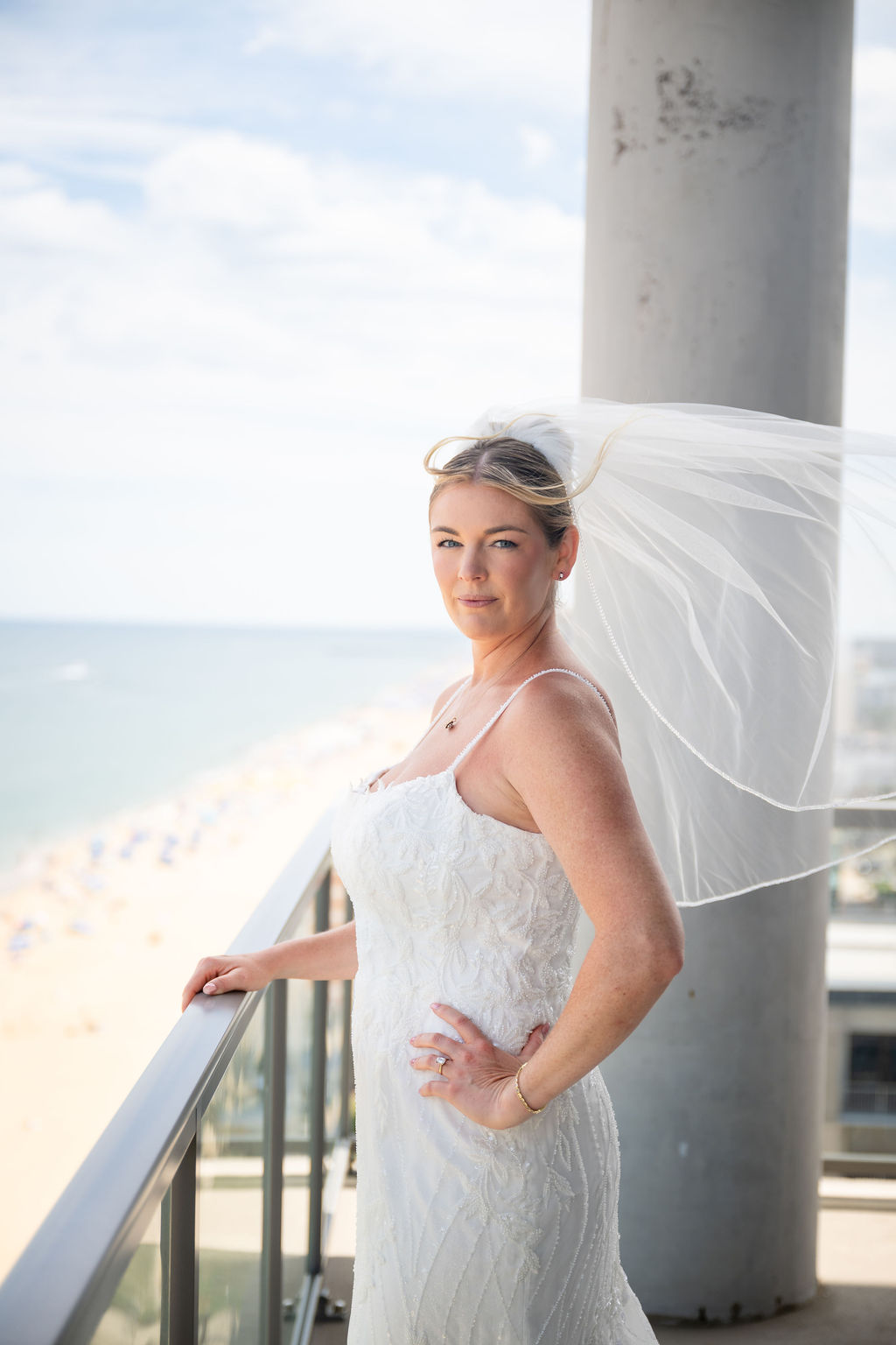 Elegant modern bridal portrait on beach oceanfront hotel balcony with veil blowing in the wind