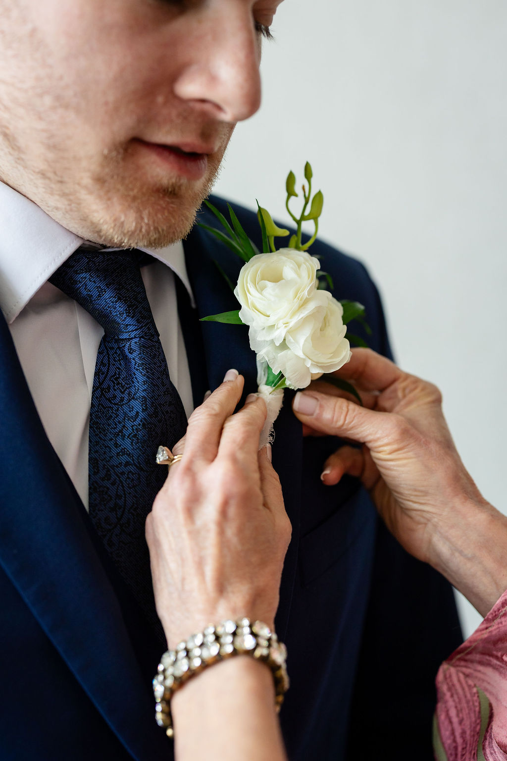 Groom putting on his all white boutonniere with ranunculus and orchids