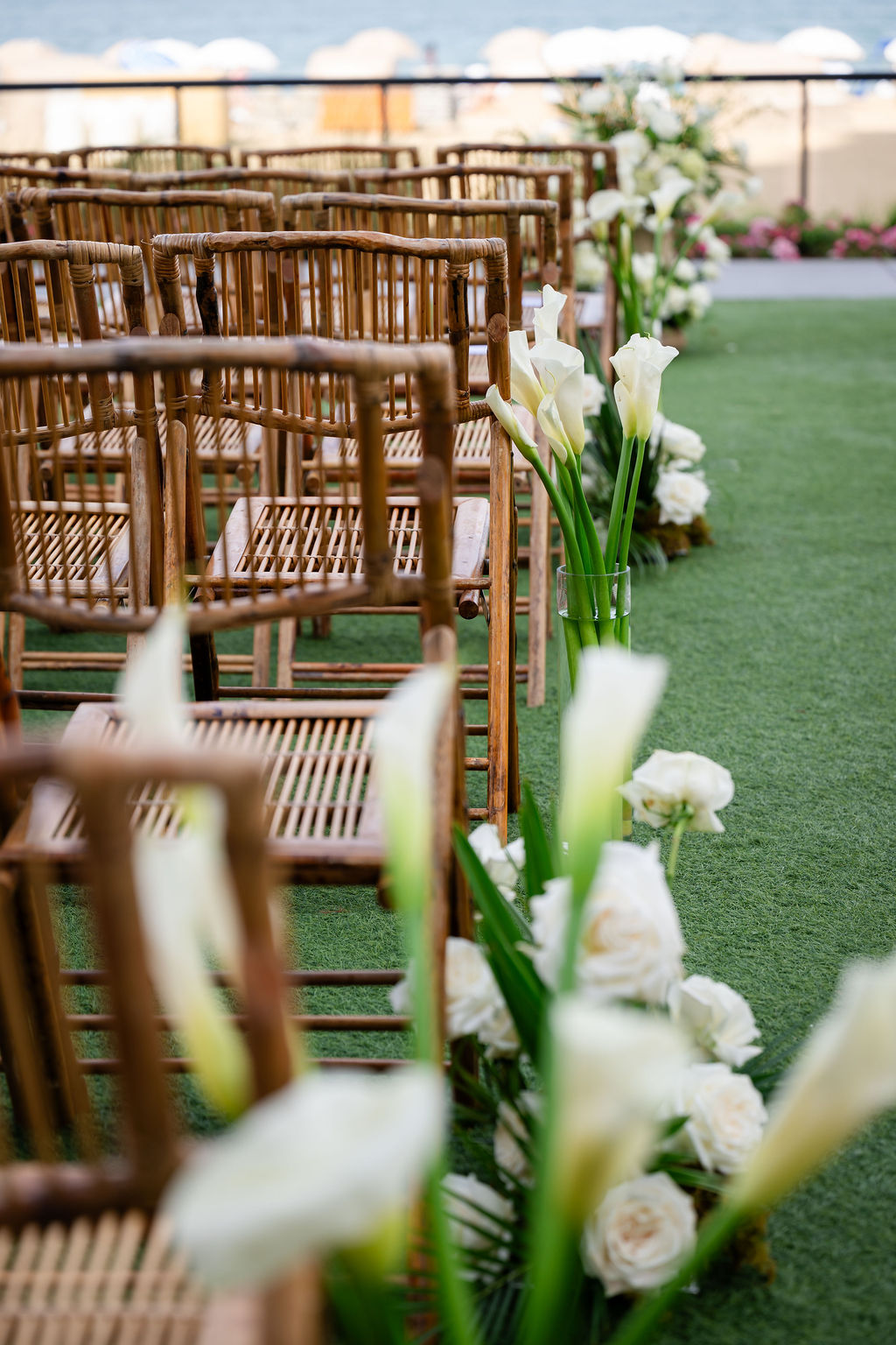 Rows of foldable bamboo chairs decorated with vases of calla lilies in the aisle for elegant beach wedding 