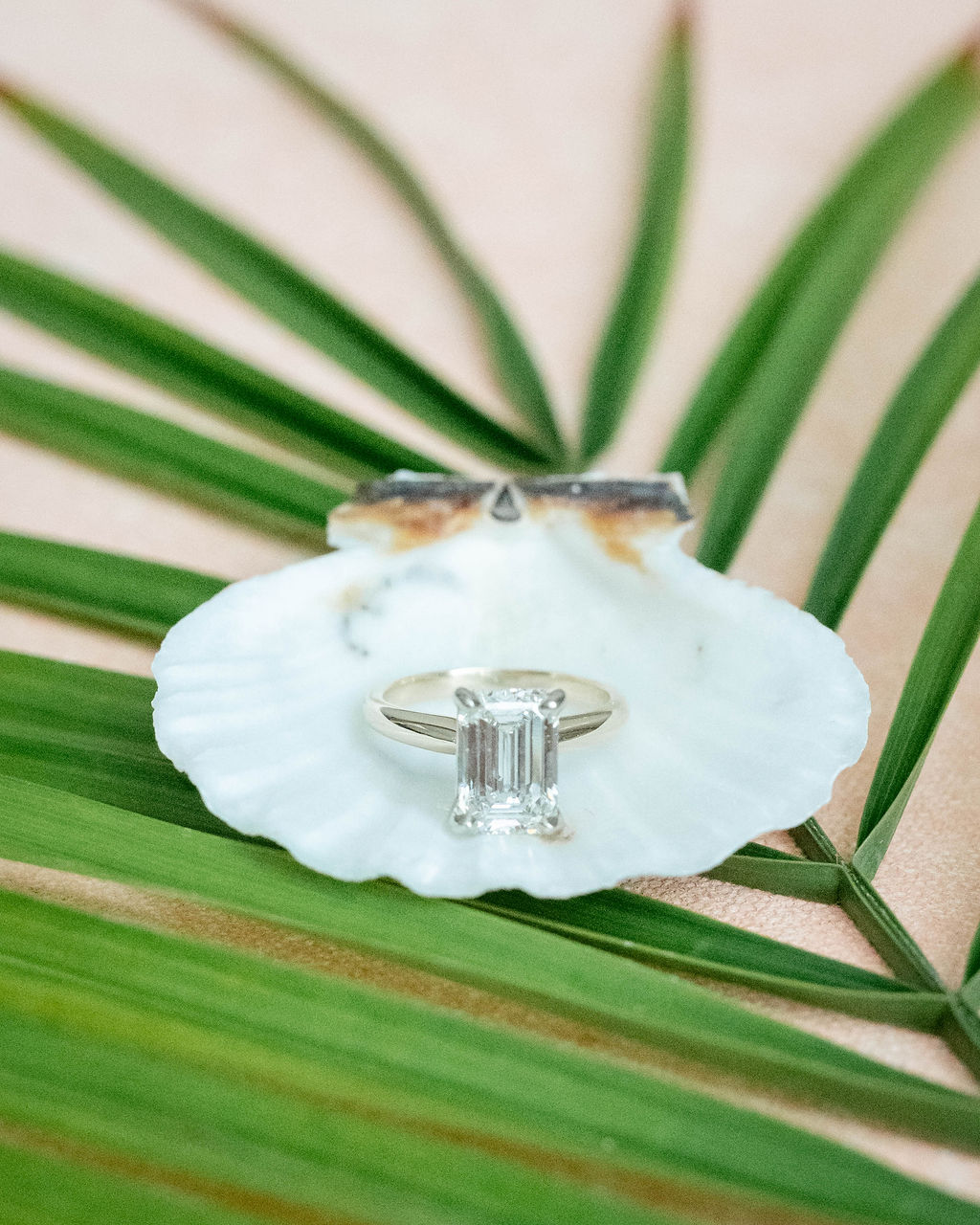 Emerald cut diamond engagement ring sitting on a seashell and palm leave for beach wedding