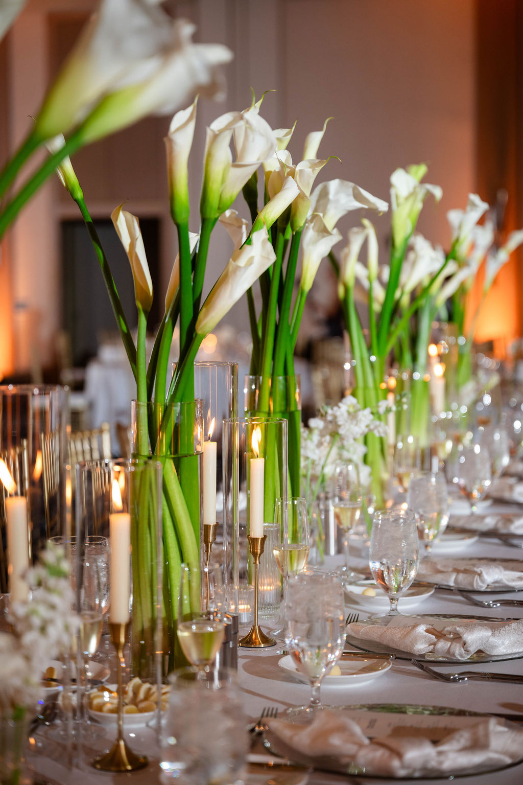 Tall rows of calla lilies and ivory candlesticks decorating beach wedding reception tables