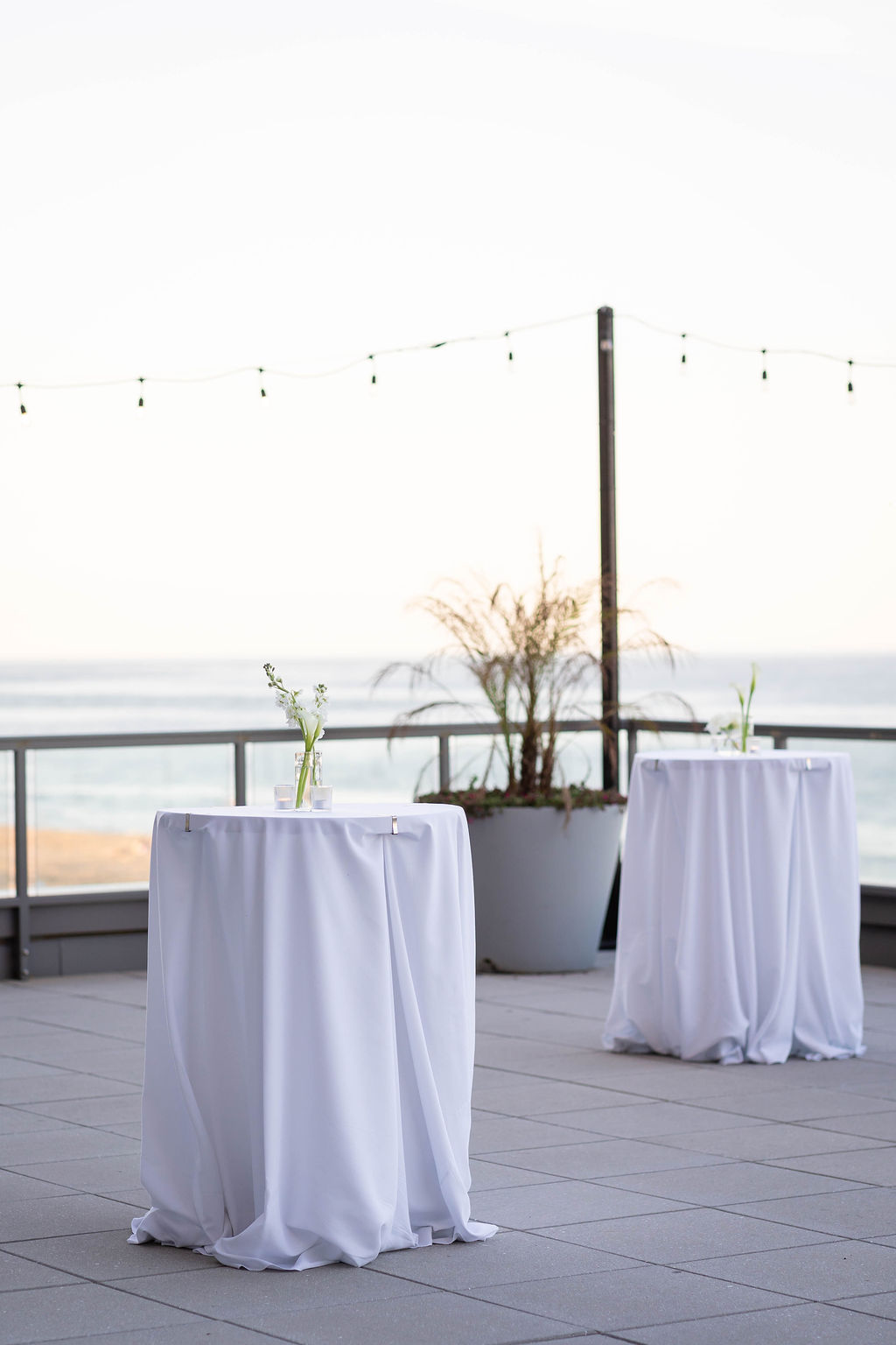 Modern cocktail hour setup with bud vases and white linens on high boy tables