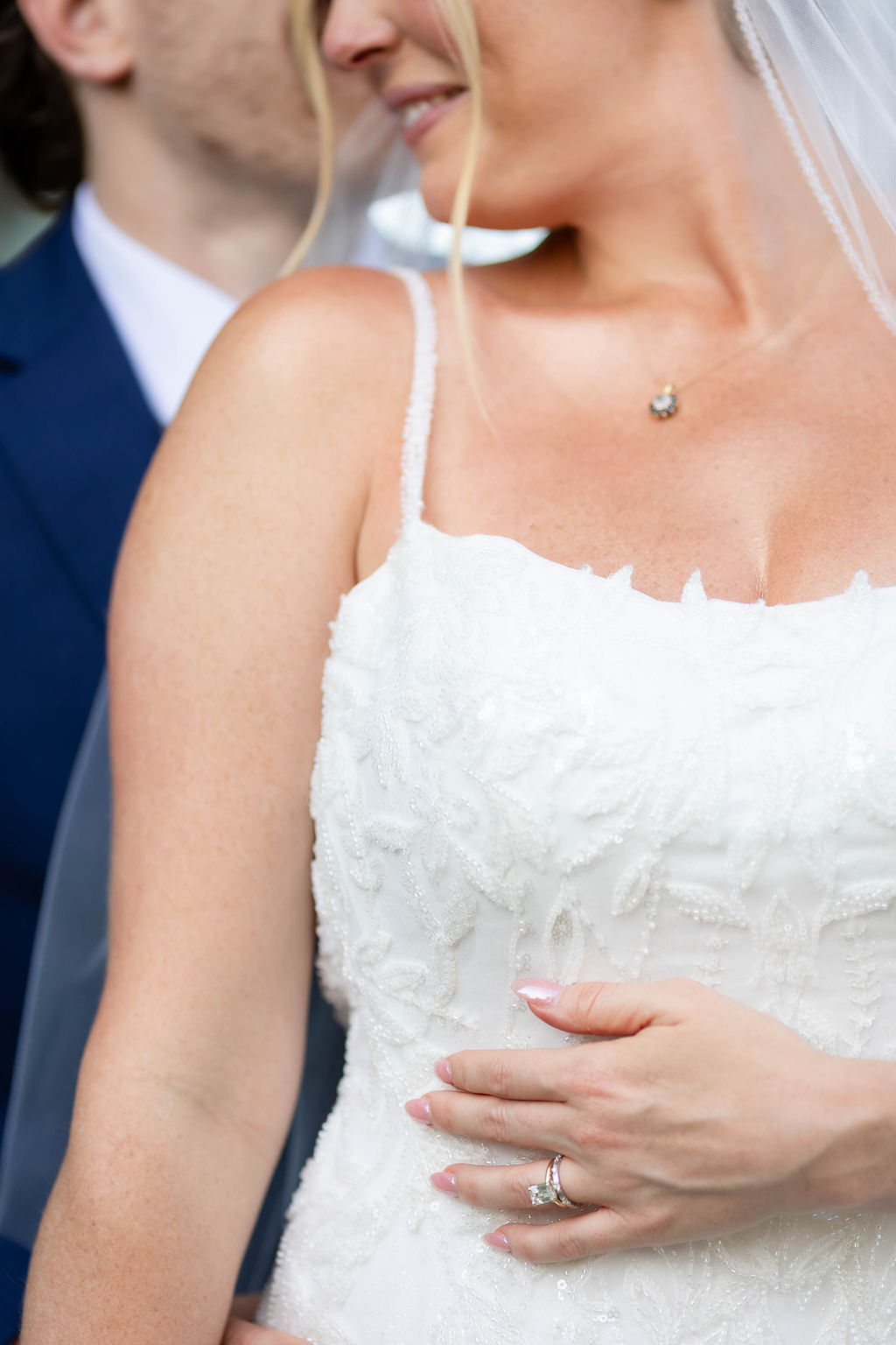 Closeup of a brides beaded wedding dress and emerald cut wedding rings