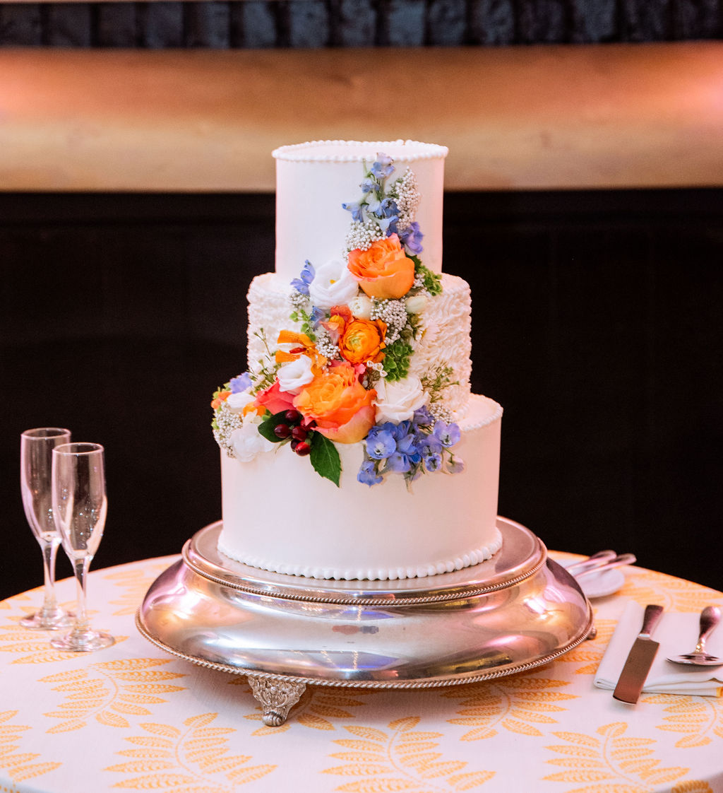 Three tiered white wedding cake with hand piped details and colorful flower decorations