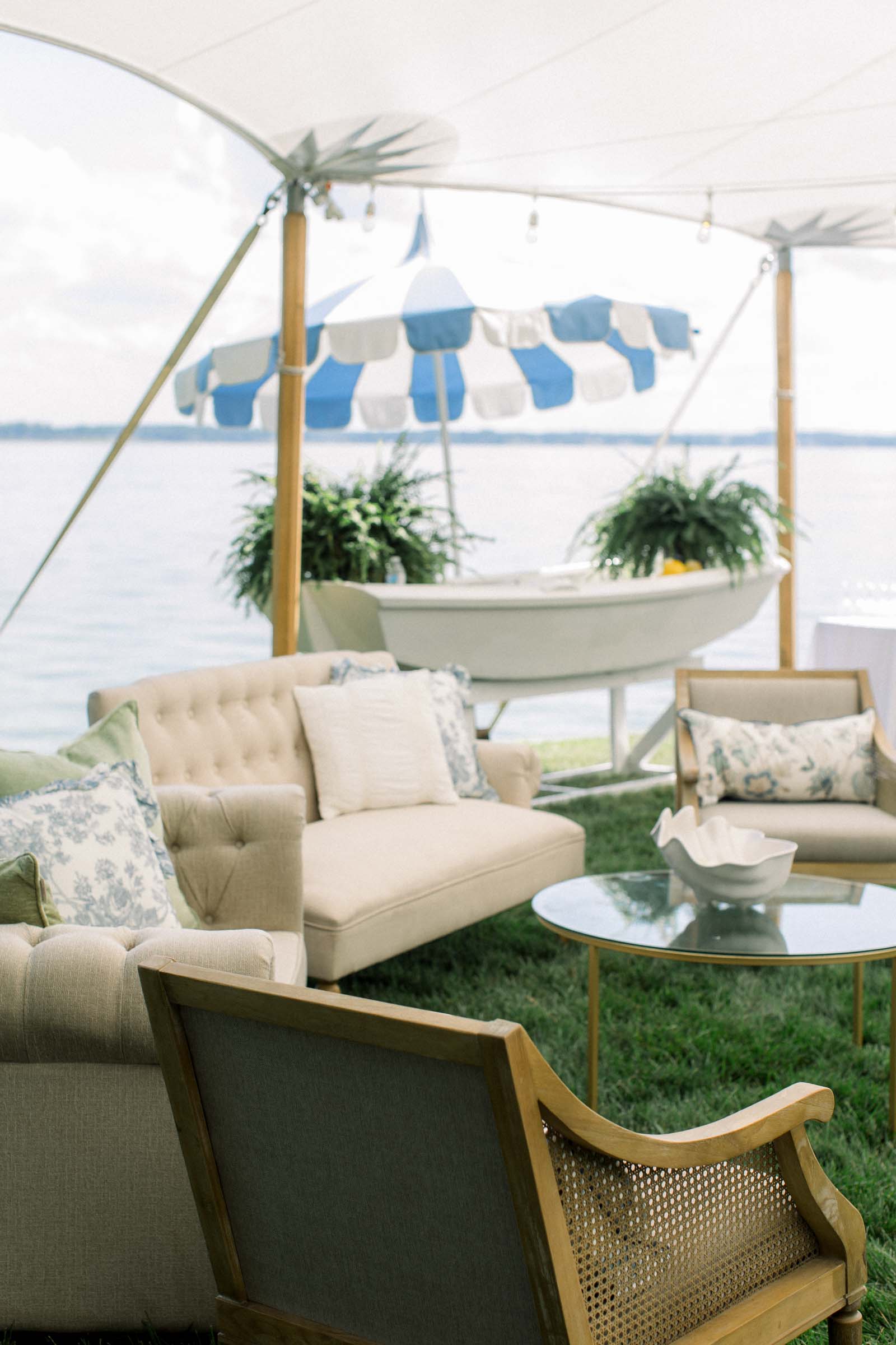 White boat used as a drinks station and lounge area with toile pillows for outdoor riverside wedding