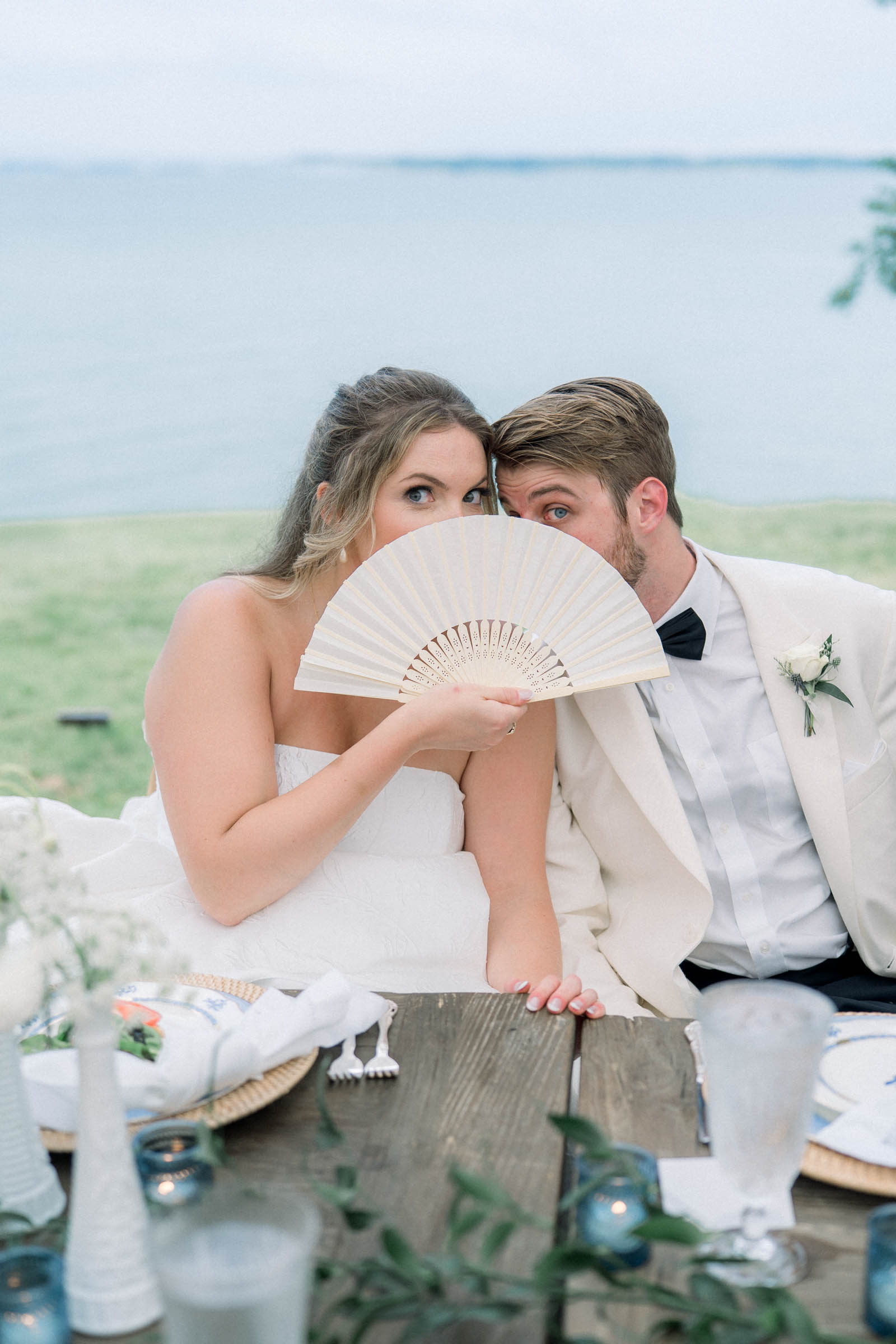 Bride and groom at their riverside Virginia wedding playfully hiding behind a fan