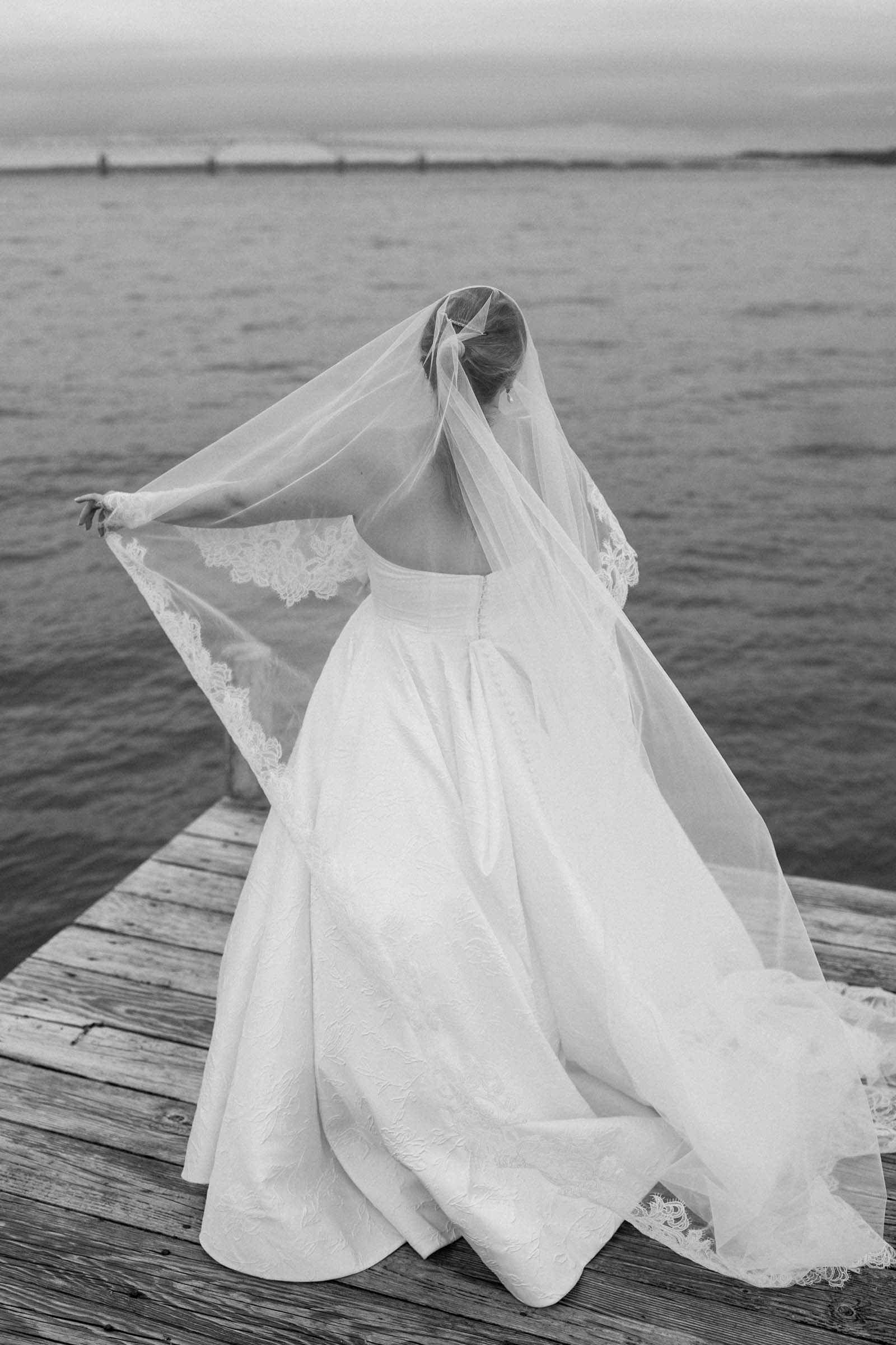 Bride with cathedral length veil edged with lace overlooking the river